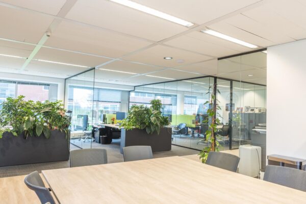 Moderne kantoorruimte aan de Tupolevlaan met glazen wanden, vergadertafel, bureaus en veel groen.