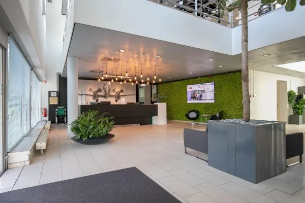 Moderne en lichte ontvangsthal aan de Tupolevlaan met een groene moswand, zitgelegenheid en een receptiebalie met vliegtuigfoto op de achtergrond.