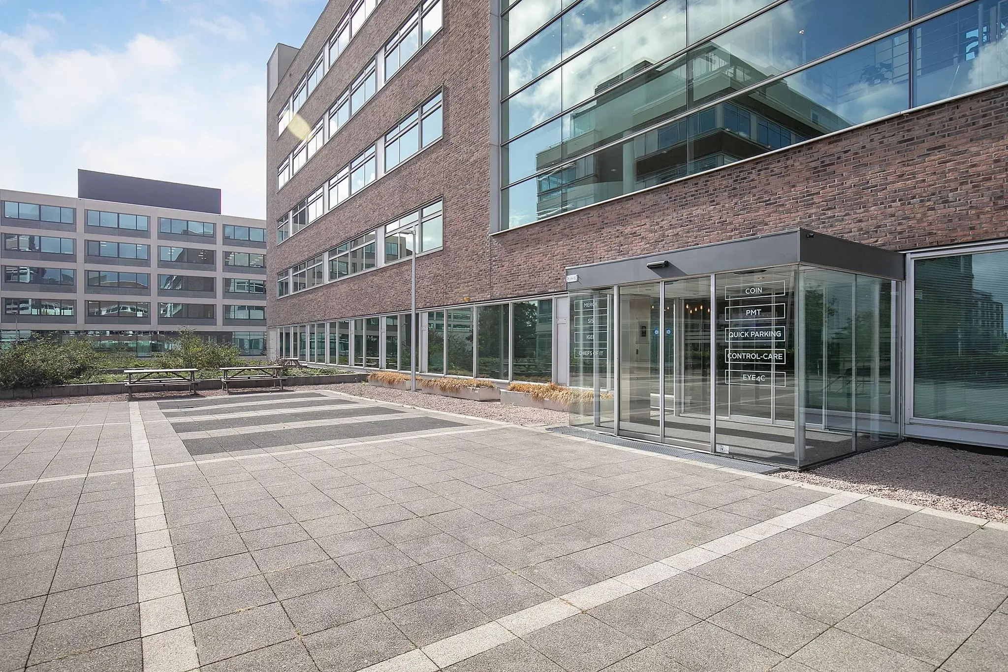 Ingang van een modern kantoorgebouw aan de Tupolevlaan met glazen entree en omliggende bestrate buitenruimte.