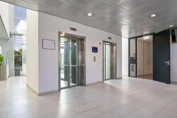 Moderne, lichte entreehal met twee liften in een kantoorgebouw aan de Tupolevlaan.