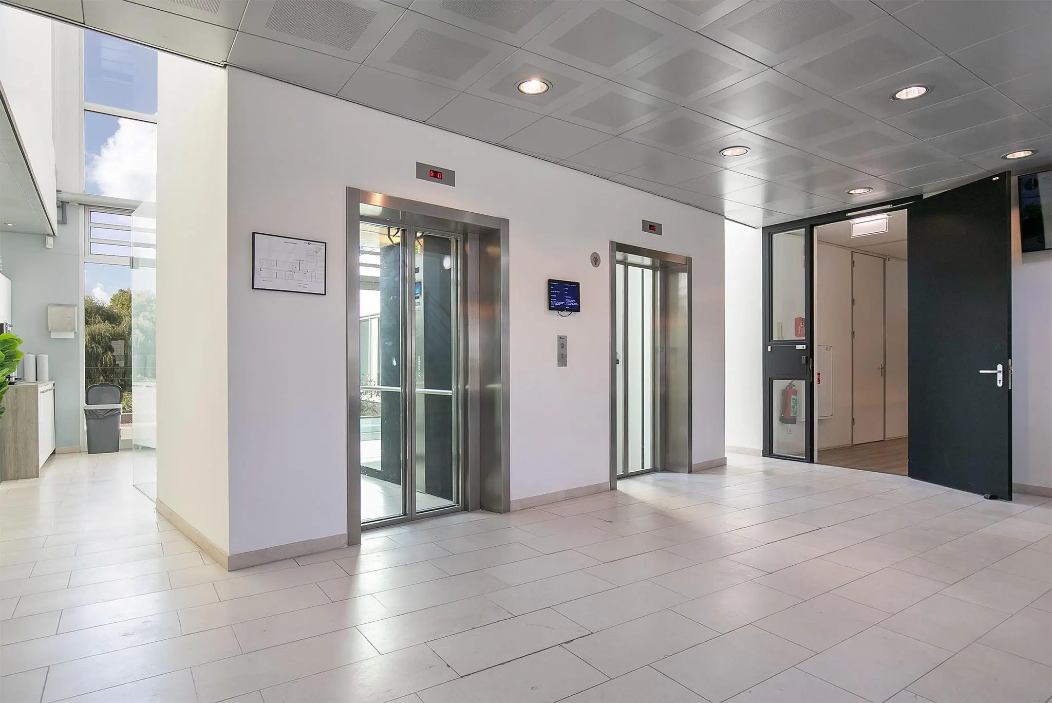 Moderne, lichte entreehal met twee liften in een kantoorgebouw aan de Tupolevlaan.