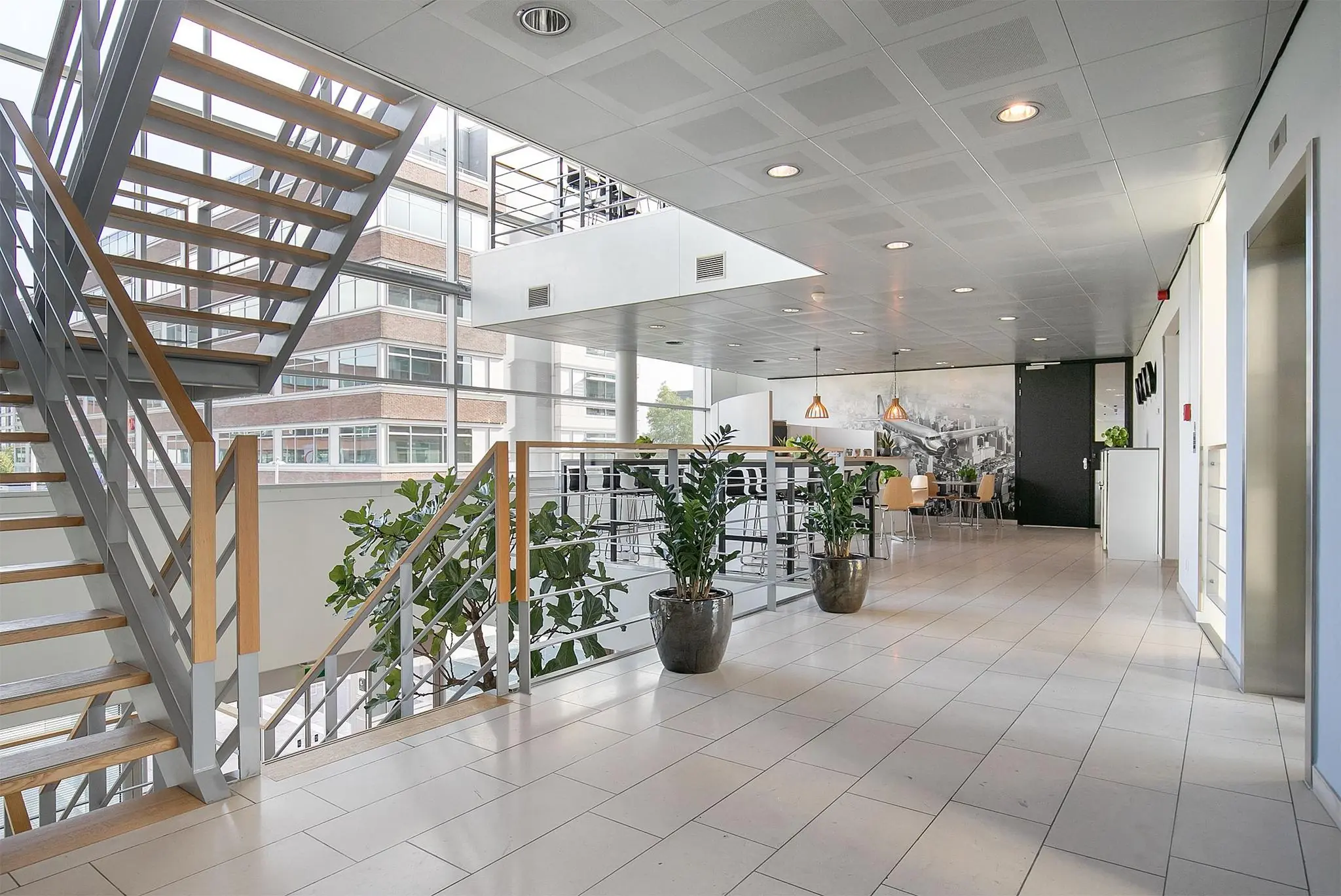 Moderne kantoorlounge aan de Tupolevlaan met open trap, zitgedeelte en grote raampartijen.