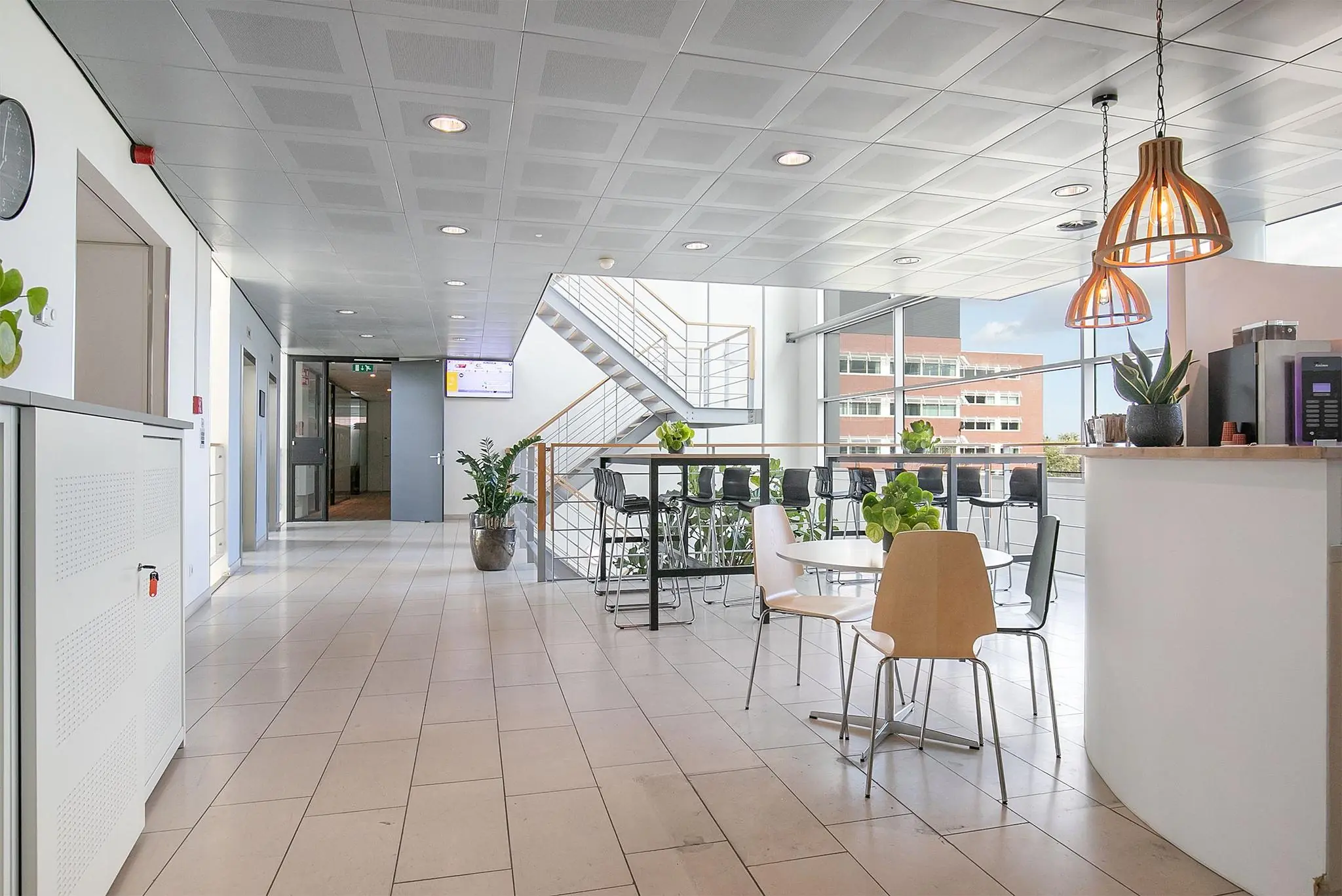 Moderne en lichte kantoorruimte aan de Tupolevlaan met zitgelegenheid, planten, een koffiehoek en een zicht op een trap en grote ramen.