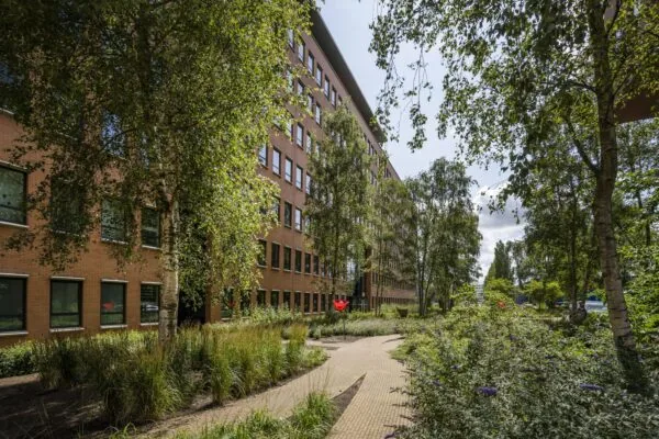 Bakstenen kantoorpand aan de Hullenbergweg met een omliggende groene tuin en wandelpad.