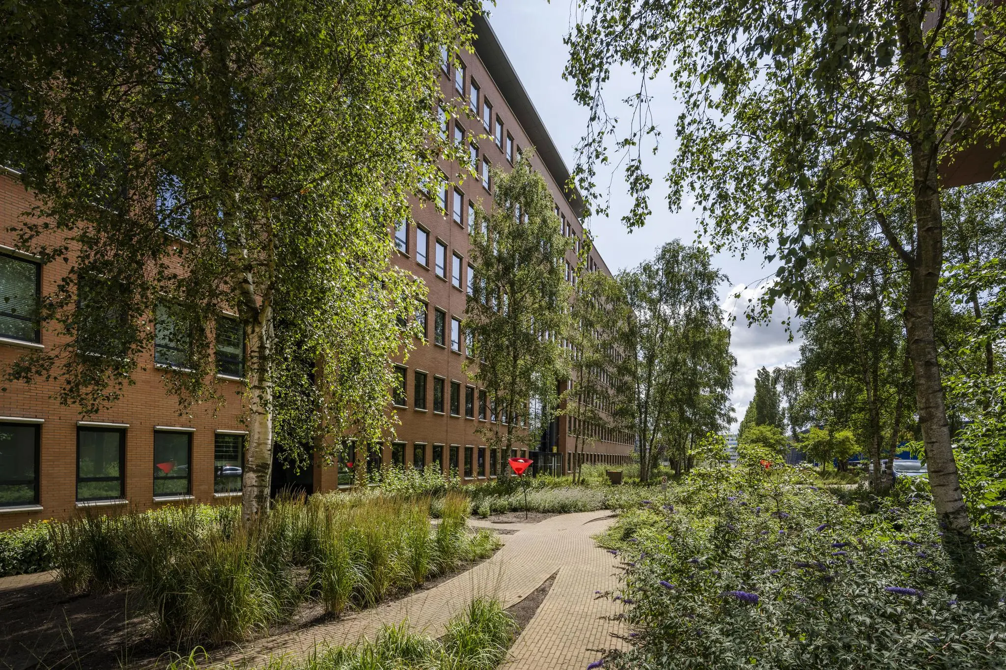 Bakstenen kantoorpand aan de Hullenbergweg met een omliggende groene tuin en wandelpad.