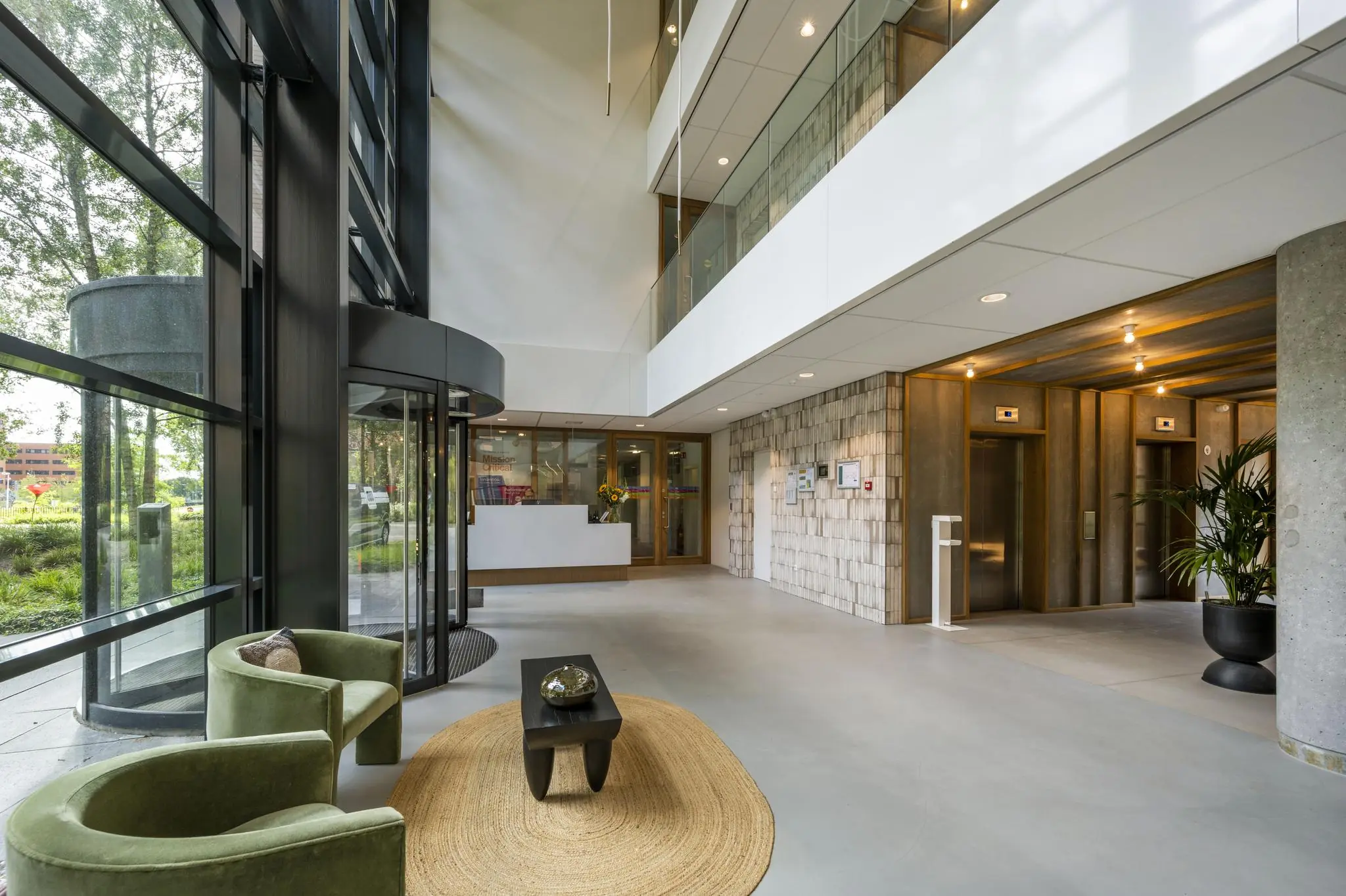 Moderne ontvangsthal van een kantoorgebouw aan de Hullenbergweg met glazen draaideur, zitgedeelte en liften.