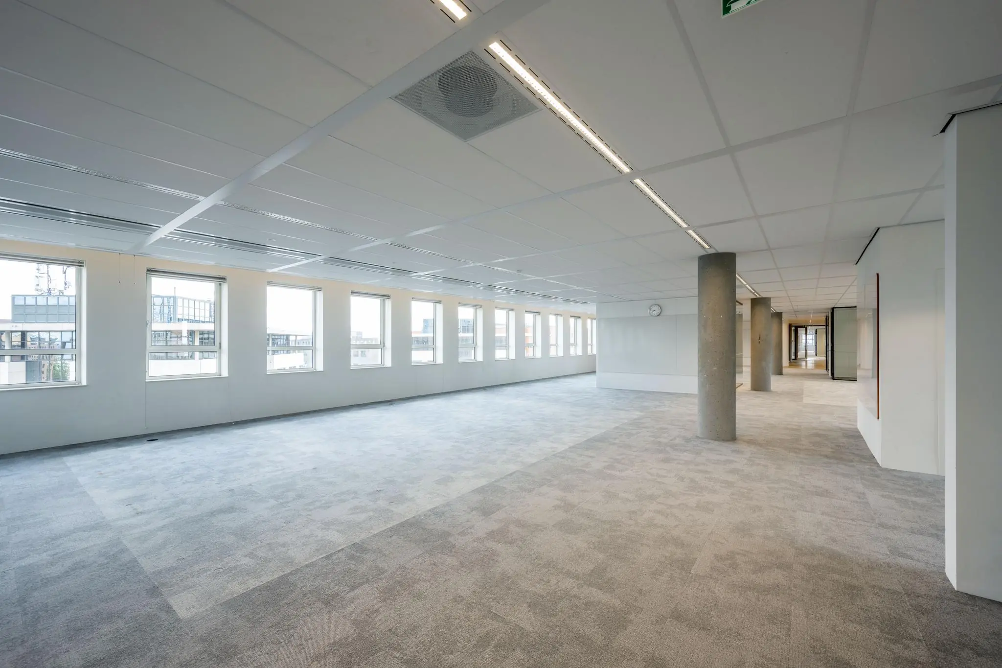Ruime, lege kantoorruimte aan de Hullenbergweg met grijze vloerbedekking, grote ramen en systeemplafond.