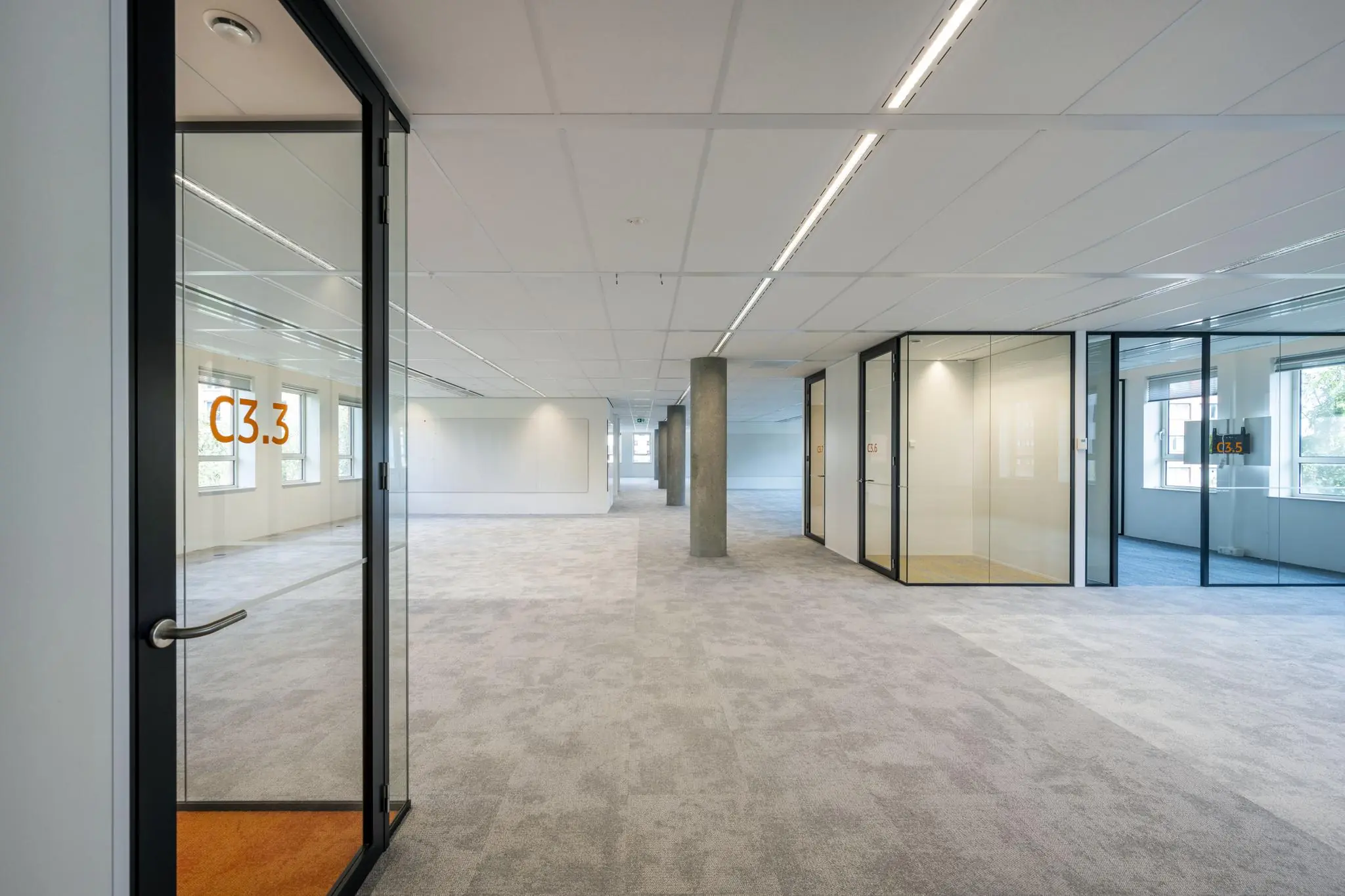 Lichte en moderne kantoorruimte aan de Hullenbergweg met glazen vergaderruimtes en grijze tapijtvloer.