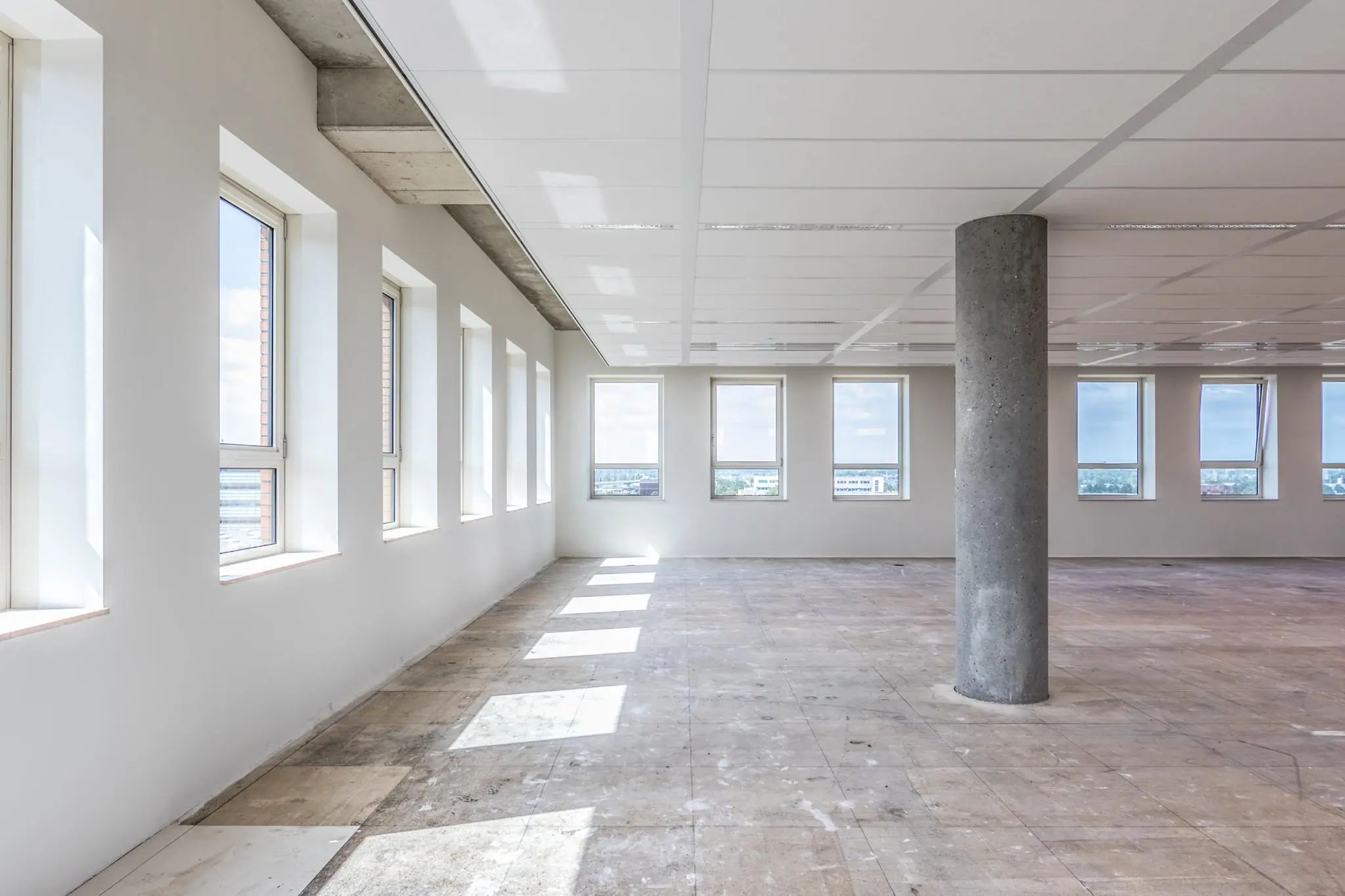 Leeg kantoorpand aan de Hullenbergweg met veel ramen en een betonnen vloer.