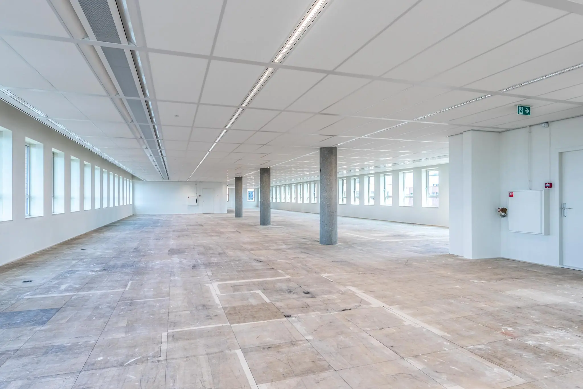 Lege kantoorruimte aan de Hullenbergweg met onafgewerkte vloer, witte plafonds en rijen ramen langs beide zijden.