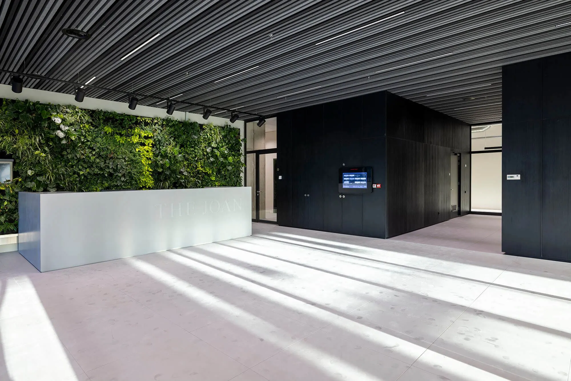 Moderne entreehal van The Joan aan de Joan Muyskenweg met een groene plantenmuur en een strakke receptiebalie.