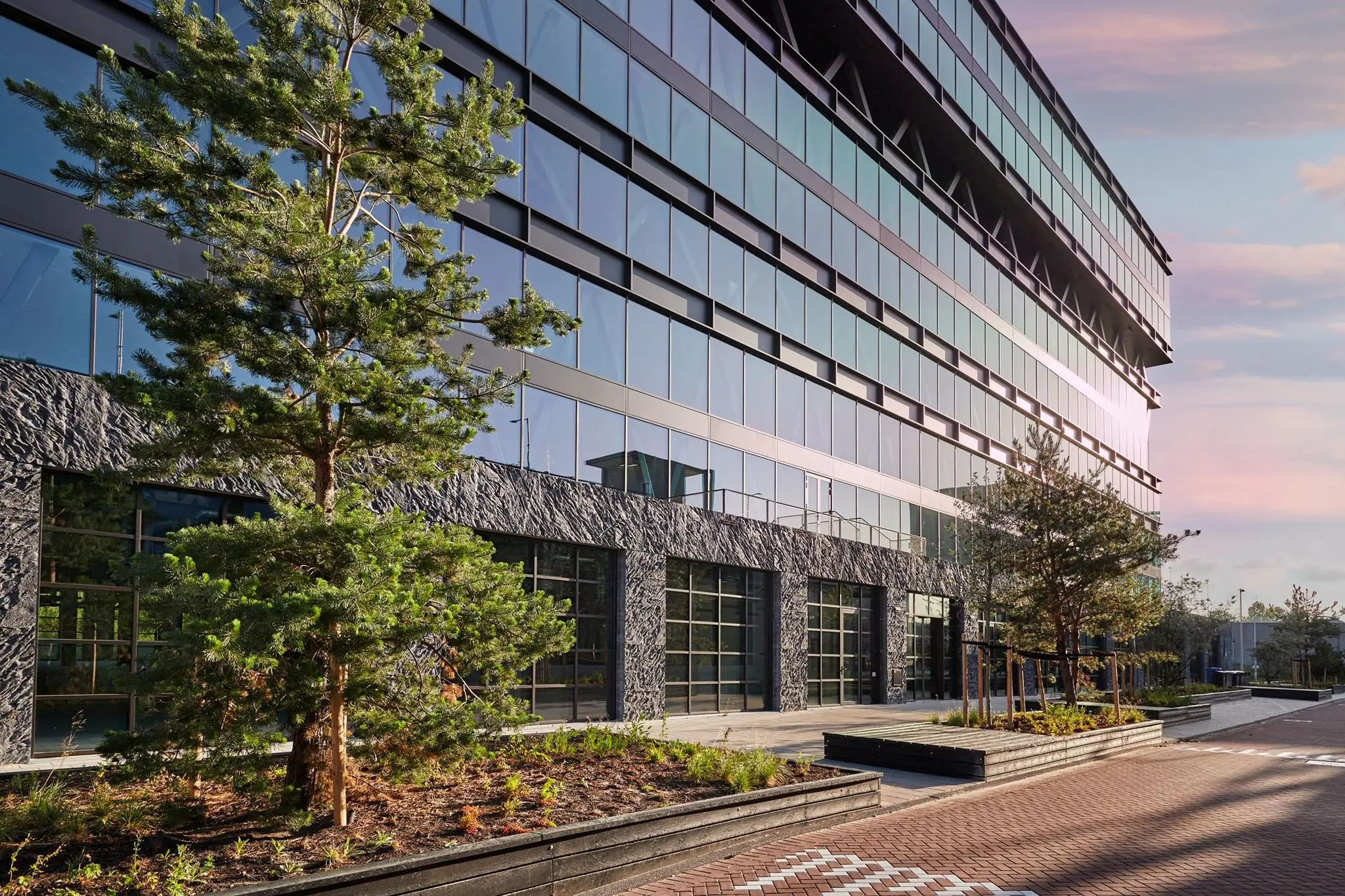 Modern kantoorgebouw aan de Joan Muyskenweg met glazen gevel en aangelegde groenstroken.