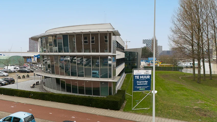 Modern kantoorgebouw aan de Sluisjesdijk met een bord "Te Huur" op de grasstrook ervoor.