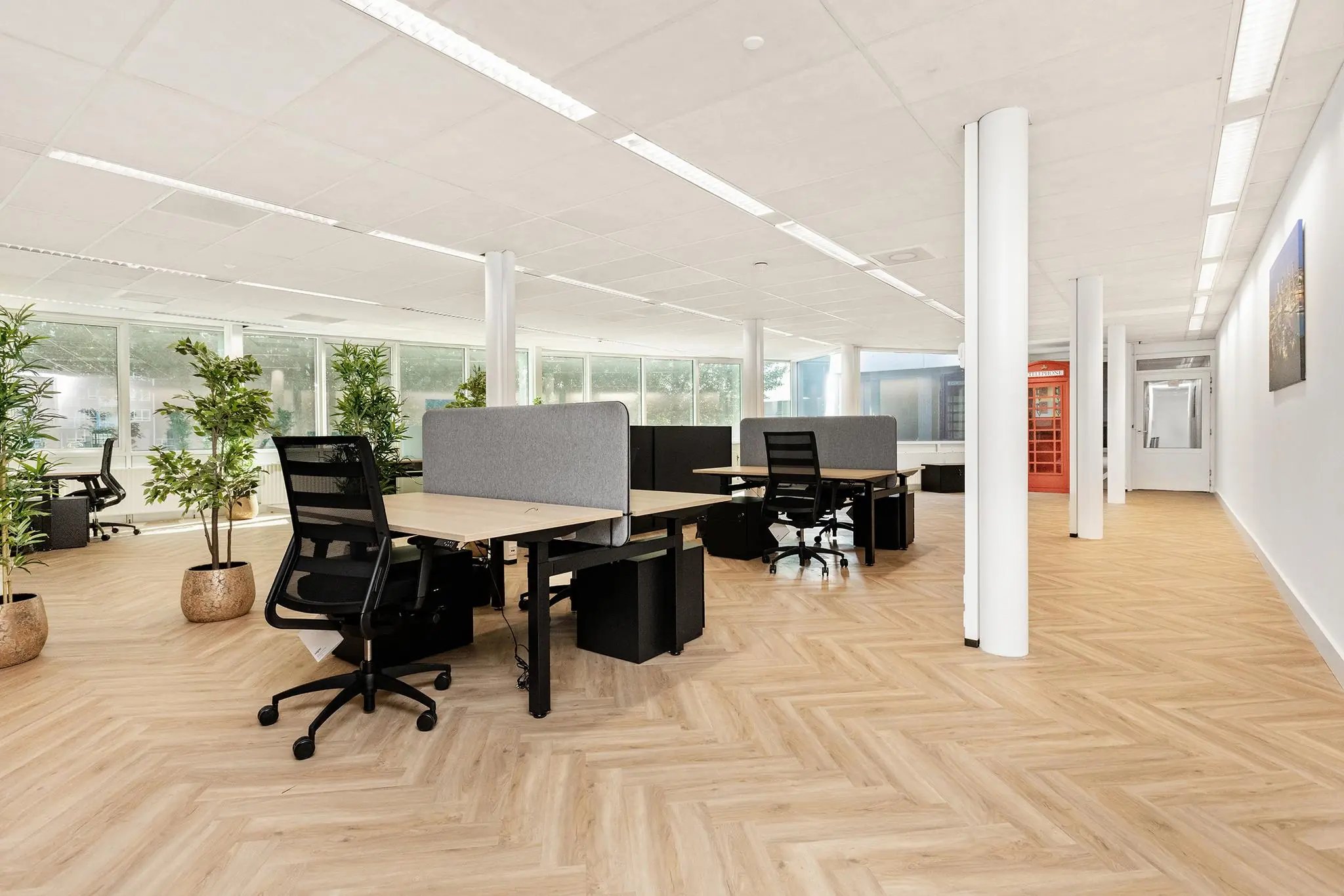 Modern en licht kantoorpand aan de Sluisjesdijk met flexwerkplekken, planten en een opvallende rode telefooncel.