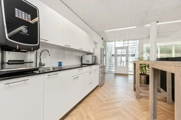 Moderne kantoorkeuken aan de Sluisjesdijk met witte kasten, een koffieautomaat en houten visgraatvloer.