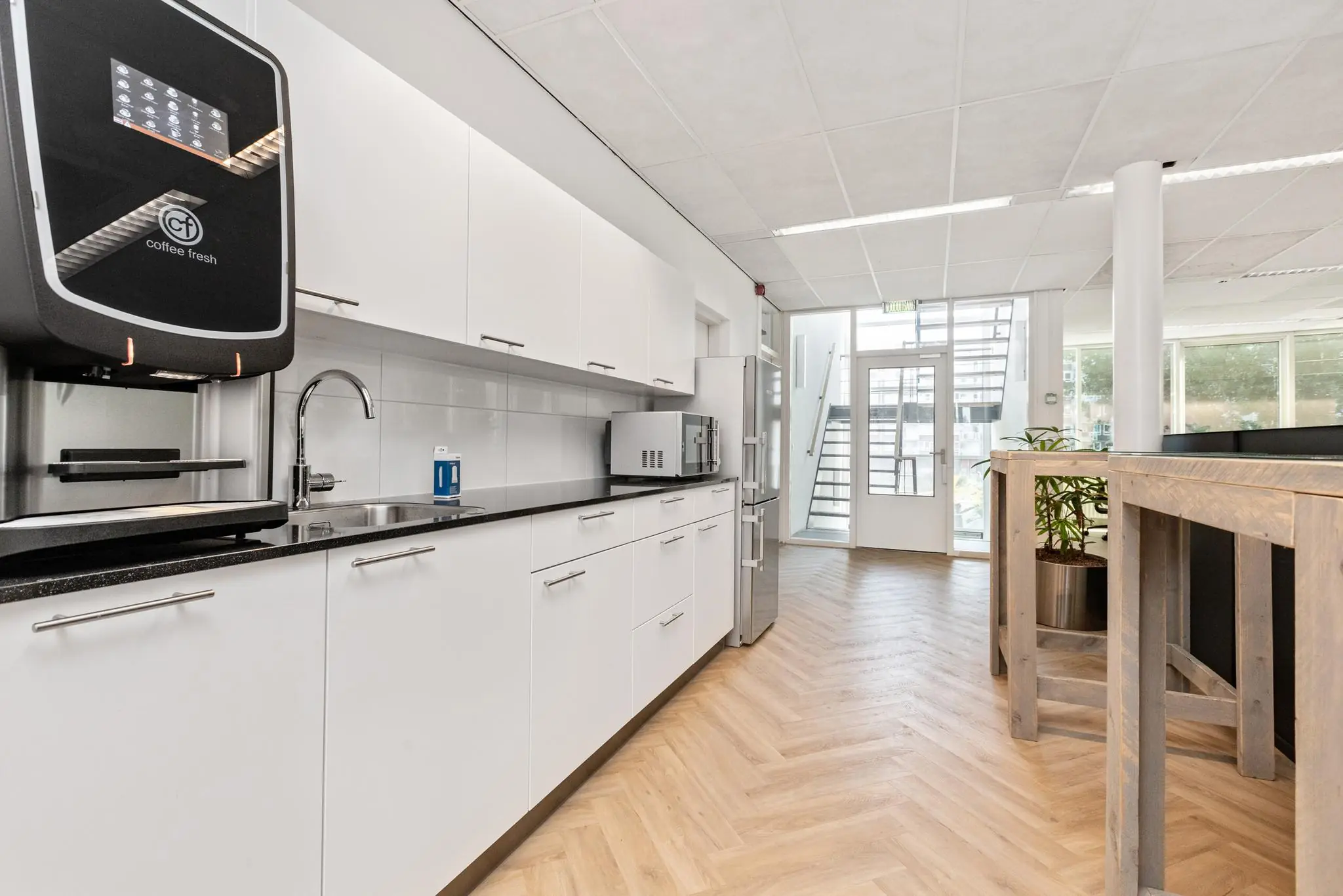 Moderne kantoorkeuken aan de Sluisjesdijk met witte kasten, een koffieautomaat en houten visgraatvloer.