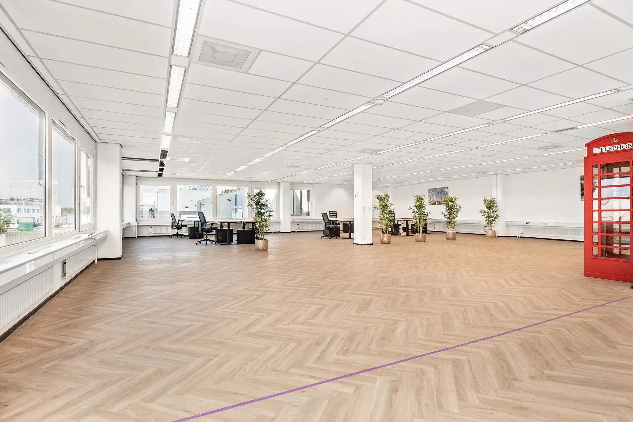 Ruim en licht kantoor aan de Sluisjesdijk met houten visgraatvloer, flexwerkplekken, planten en een rode telefooncel.