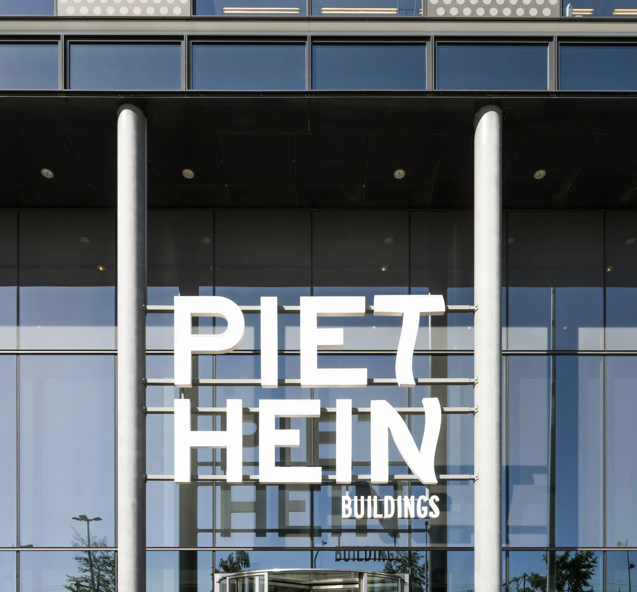 Glazen gevel van het Piet Hein Buildings-kantoor met grote witte belettering op de ingang.