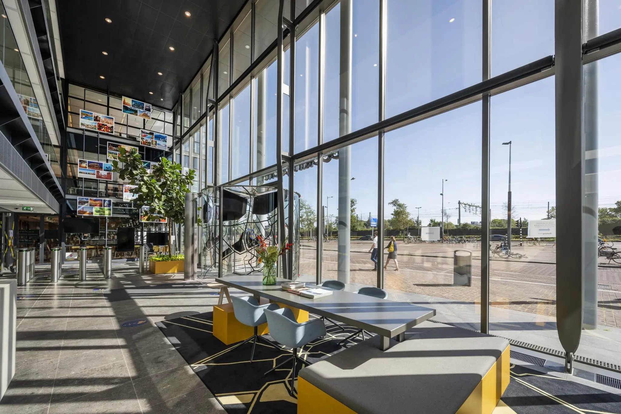 Moderne, lichte lobby aan de Piet Heinkade met hoge ramen, kleurrijke zitplekken en uitzicht op het stationsgebied.