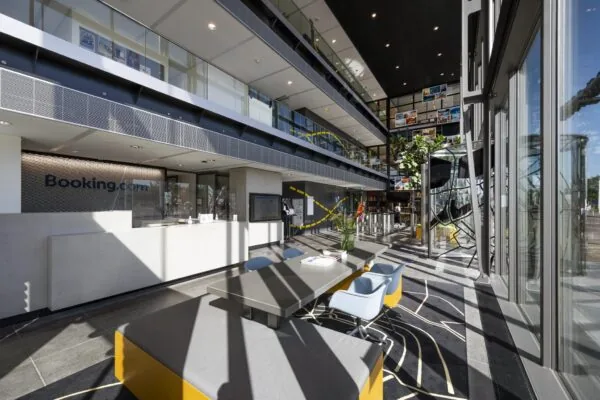 Moderne, zonovergoten entreehal van het Booking.com-kantoor aan de Piet Heinkade in Amsterdam met receptie, zitgedeelte en glazen gevel.