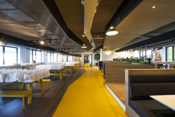 Moderne en ruime bedrijfskantine aan de Piet Heinkade met gele looppaden, picknicktafels vol lunchpakketten en groene zithoeken.