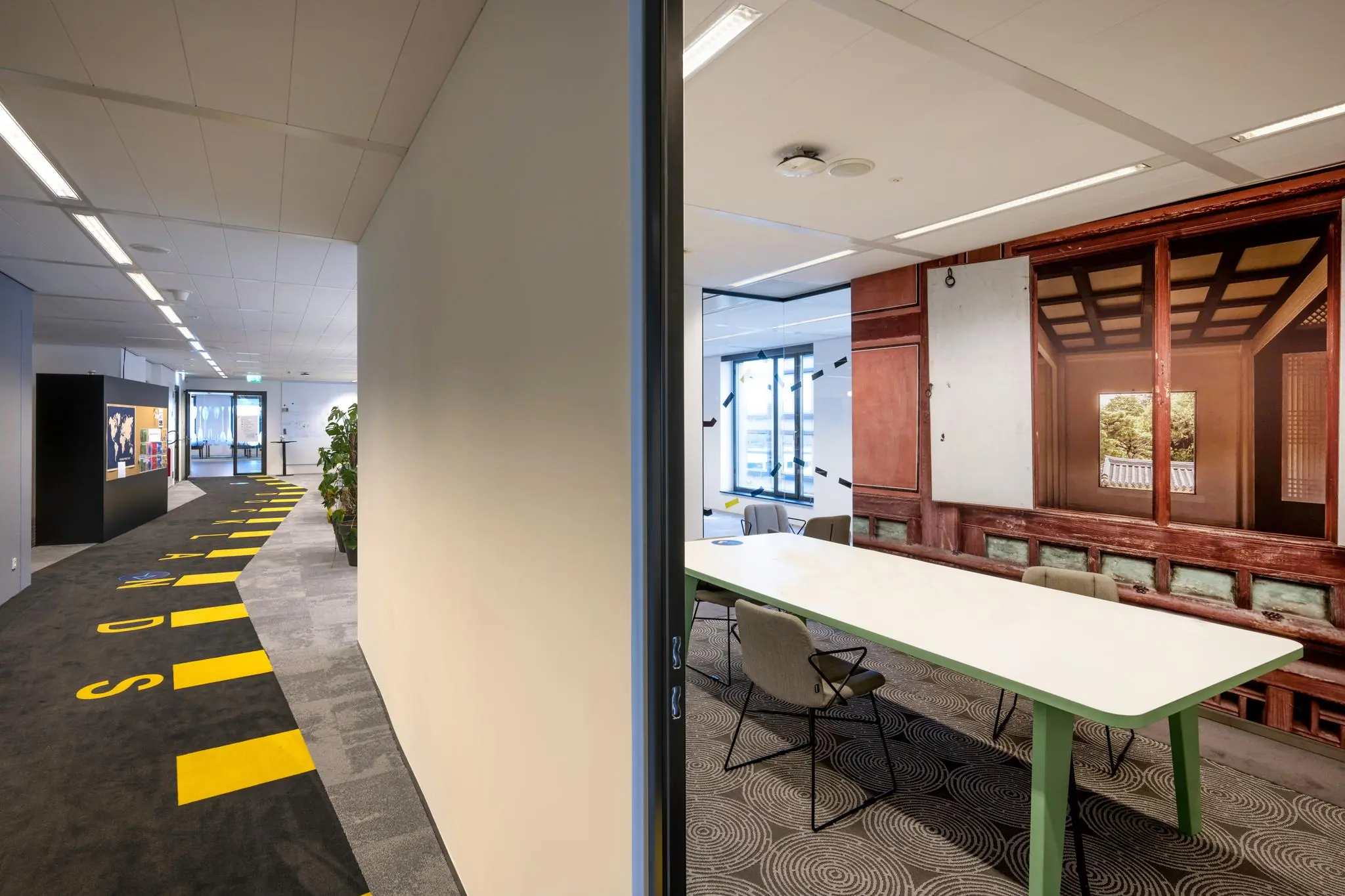 Kantoorinterieur aan de Piet Heinkade met zicht op een gang met opvallende vloerbedrukking en een vergaderruimte met grote wandfoto van een traditioneel Aziatisch interieur.