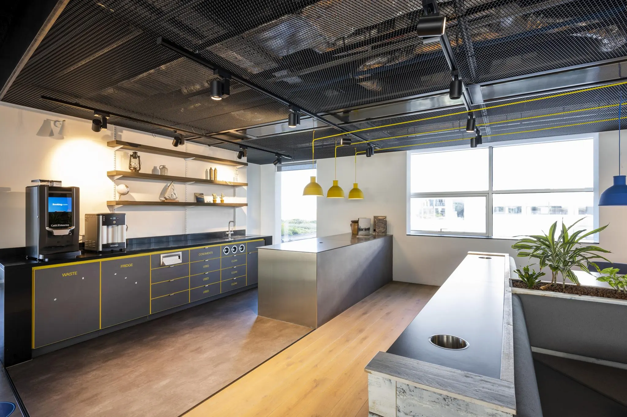 Moderne kantoorkeuken aan de Piet Heinkade met strak design, koffieapparaat, werkblad en zithoek met planten.