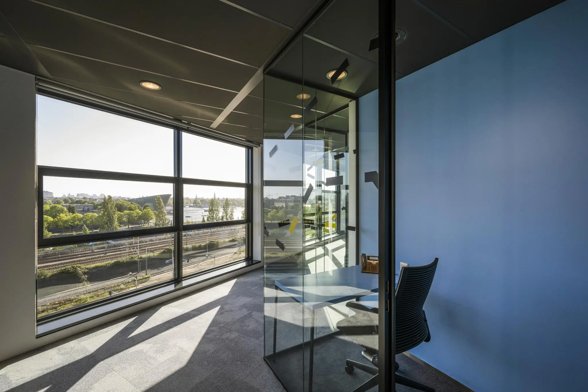 Modern glazen kantoorkamertje aan de Piet Heinkade met uitzicht op het spoor en het IJ in Amsterdam.