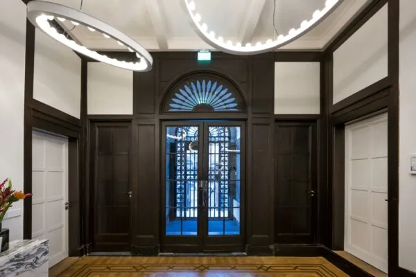 Entreehal aan de Honthorststraat met houten wandpanelen, glazen dubbele deur en moderne ronde plafondlampen.