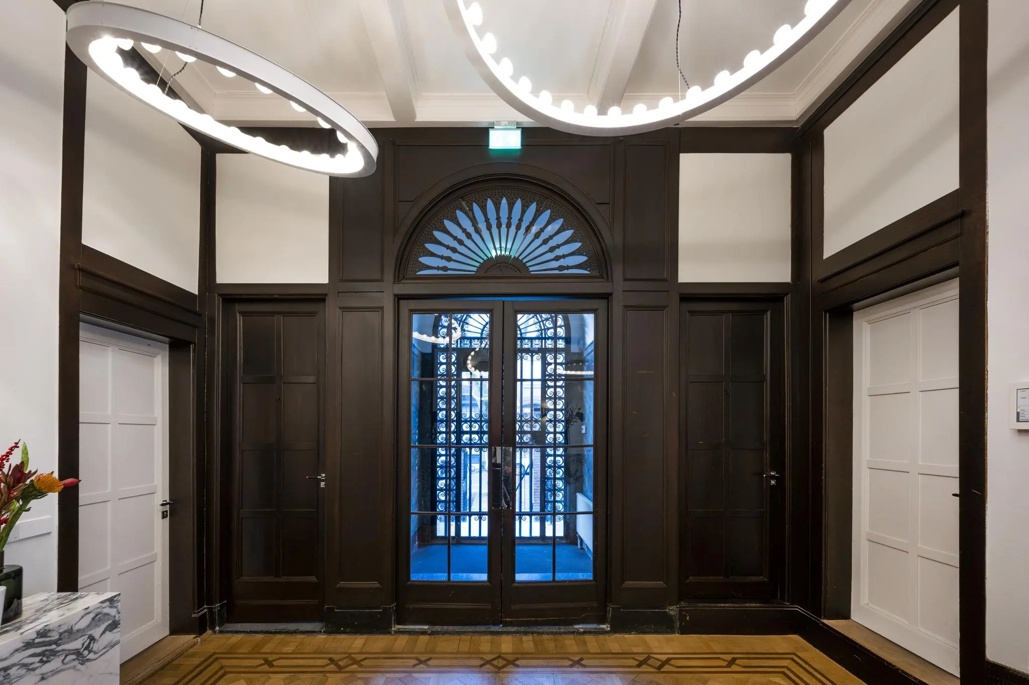 Entreehal aan de Honthorststraat met houten wandpanelen, glazen dubbele deur en moderne ronde plafondlampen.