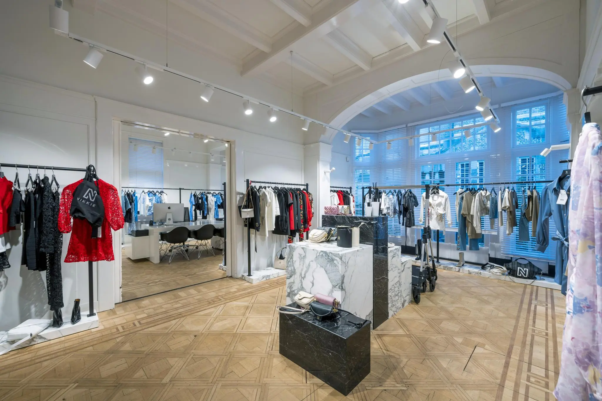 Moderne kledingwinkel aan de Honthorststraat met stijlvolle damesmode, marmeren displays en houten visgraatvloer.
