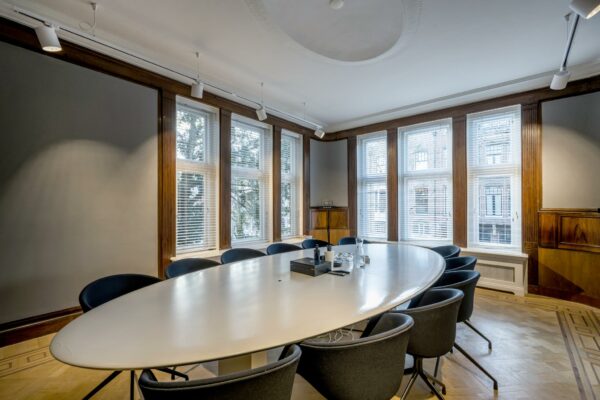 Vergaderruimte met ovale tafel, moderne stoelen en grote ramen aan de Honthorststraat.