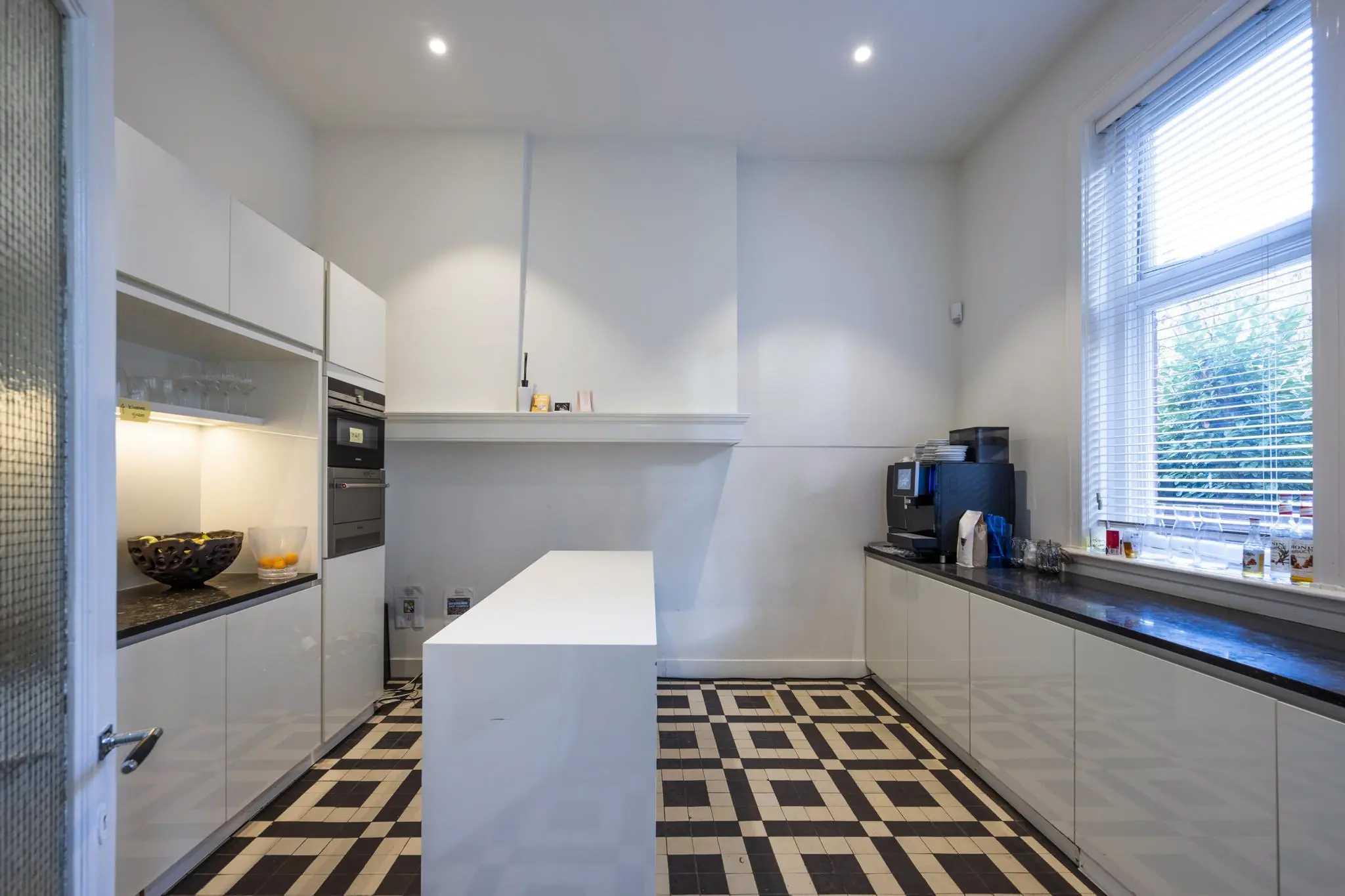 Moderne witte keuken aan de Honthorststraat met zwart-wit tegelvloer, keukeneiland en groot raam.