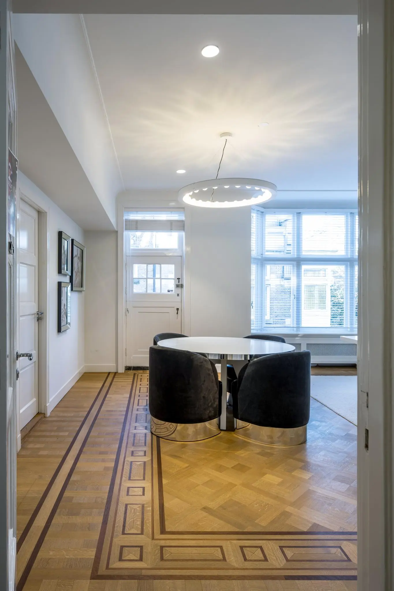 Moderne eetkamer aan de Honthorststraat met ronde tafel, vier zwarte stoelen en een houten vloer met inlegpatroon.