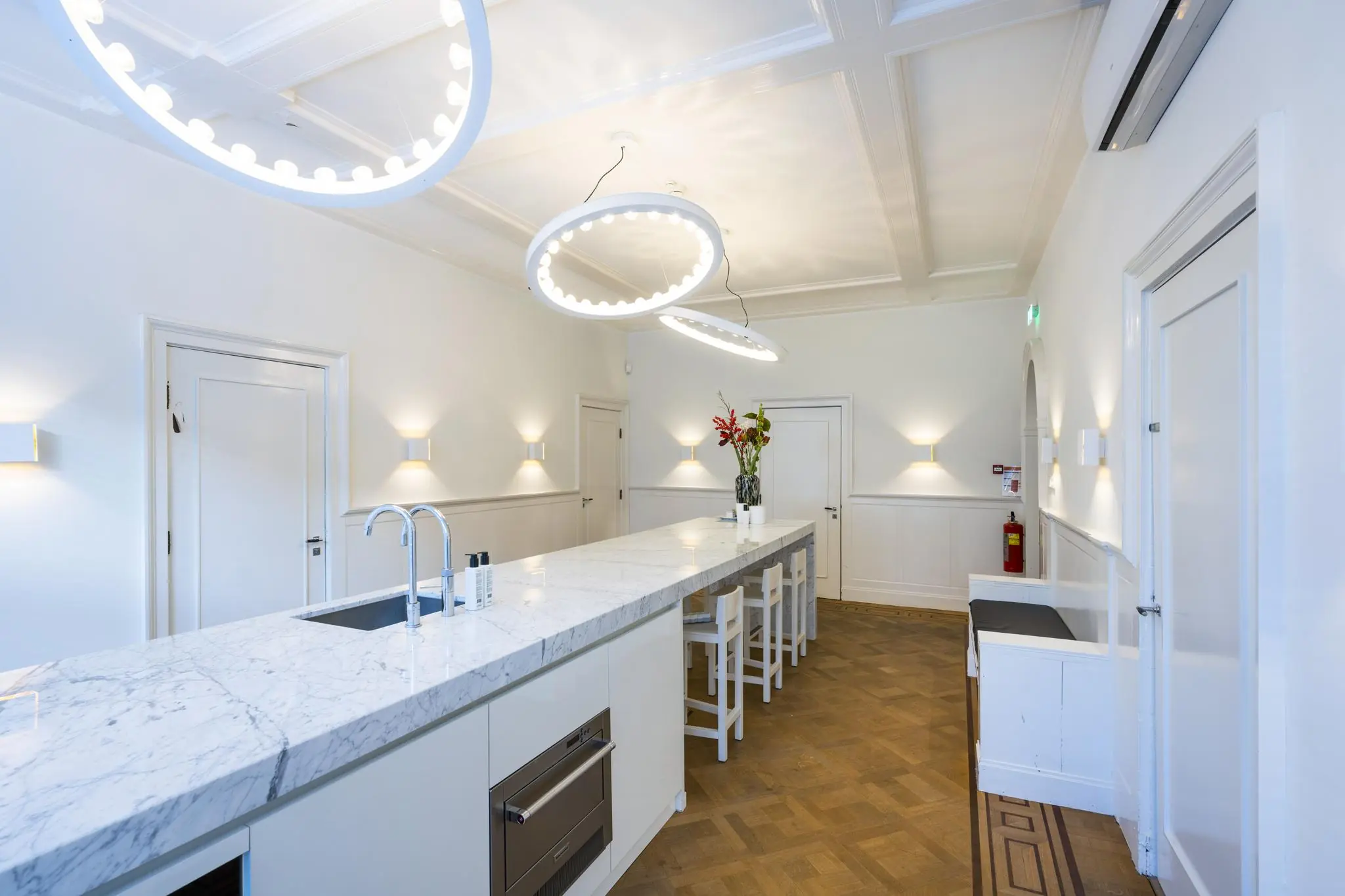 Moderne, wit ingerichte keuken aan de Honthorststraat met een marmeren kookeiland en opvallende ronde plafondlampen.