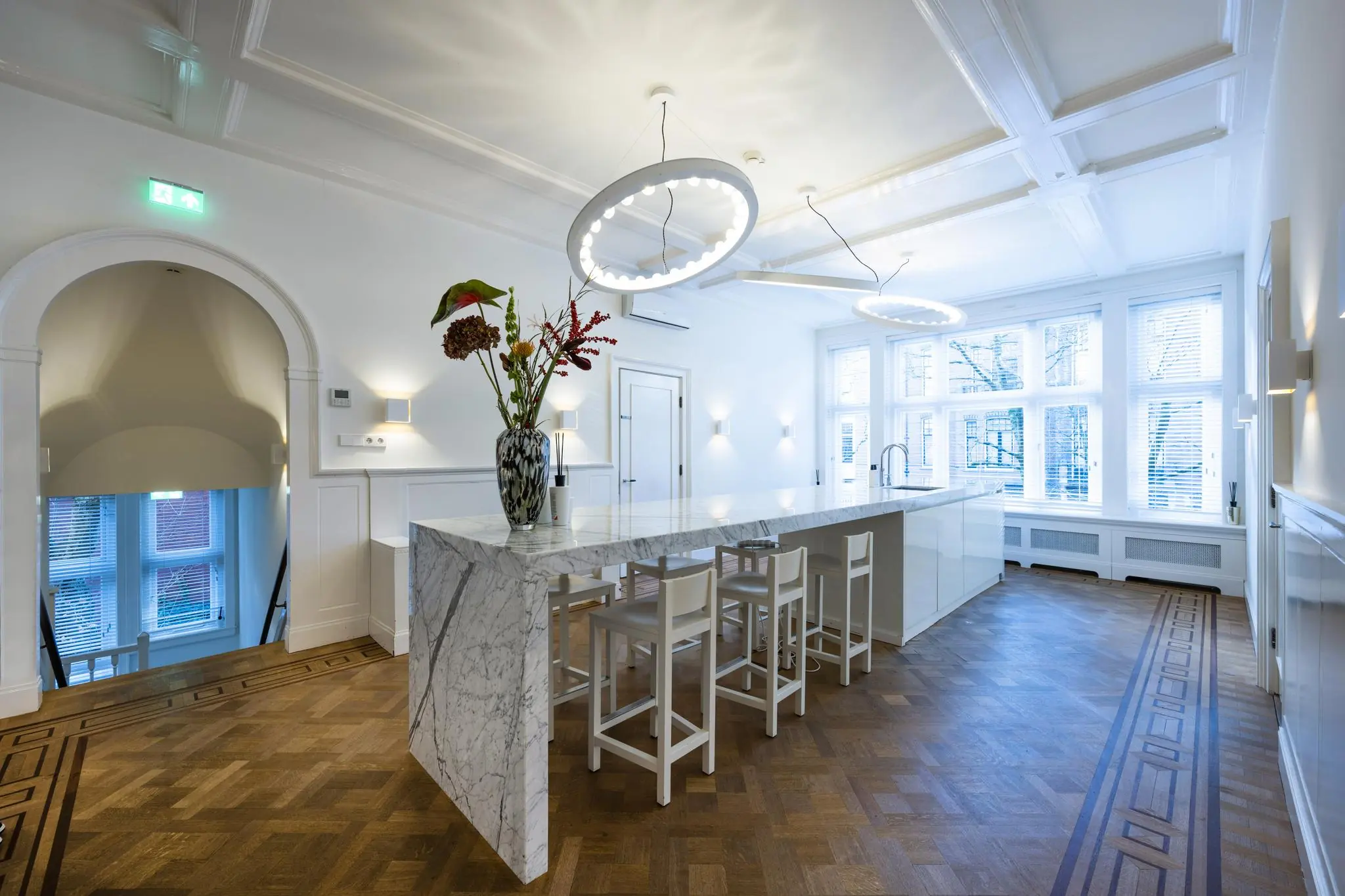 Moderne, lichte keuken aan de Honthorststraat met een marmeren kookeiland, houten visgraatvloer en grote ramen.