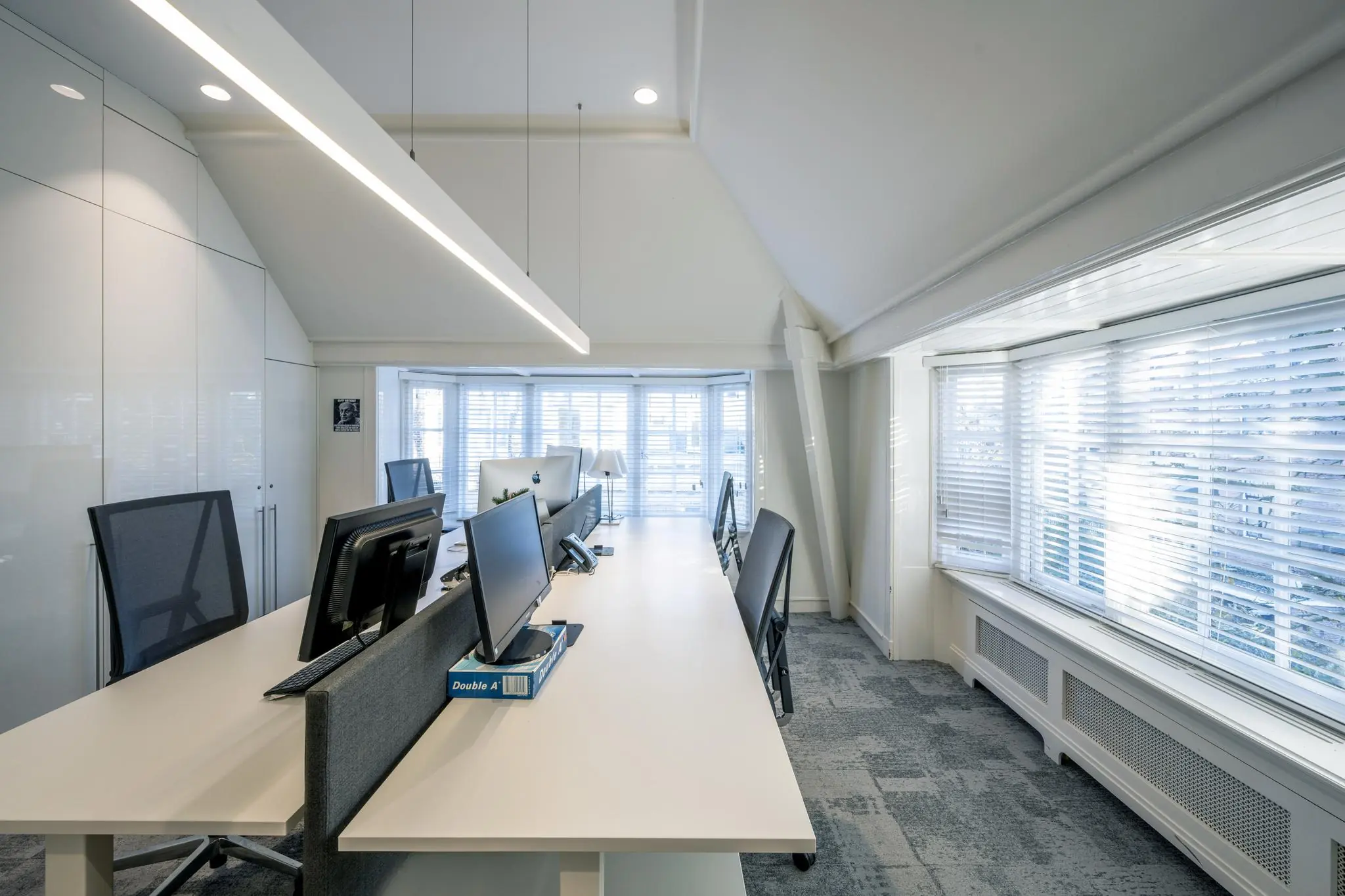 Modern en licht kantoorinterieur aan de Honthorststraat met meerdere werkplekken, computers en grote ramen met jaloezieën.