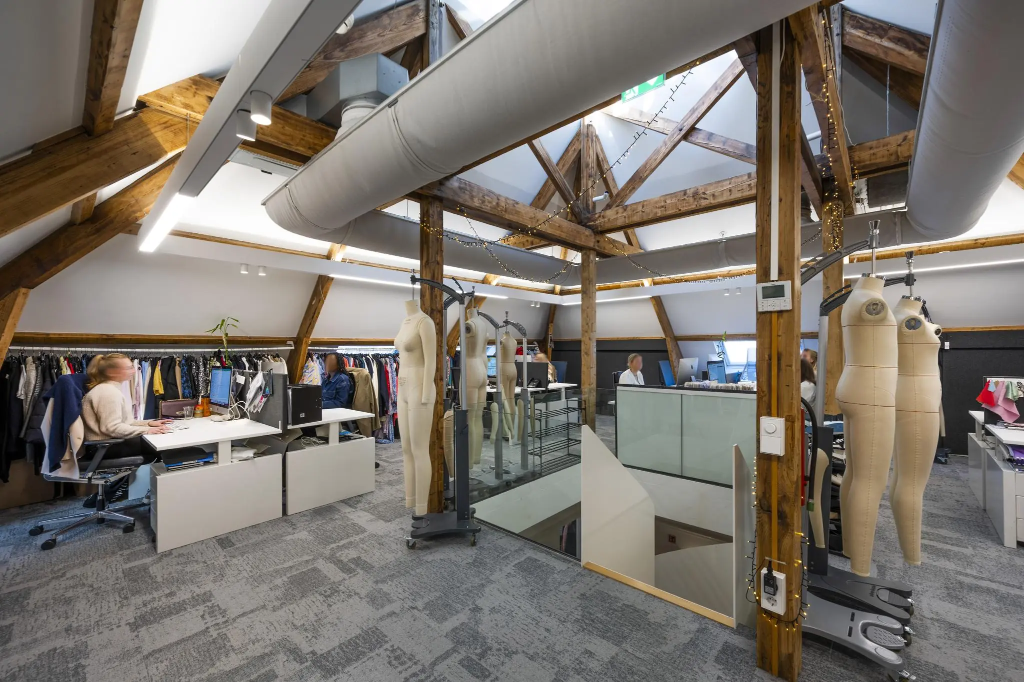 Modern modekantoor aan de Honthorststraat met zicht op werkplekken, paspoppen en kledingrekken onder houten dakspanten.