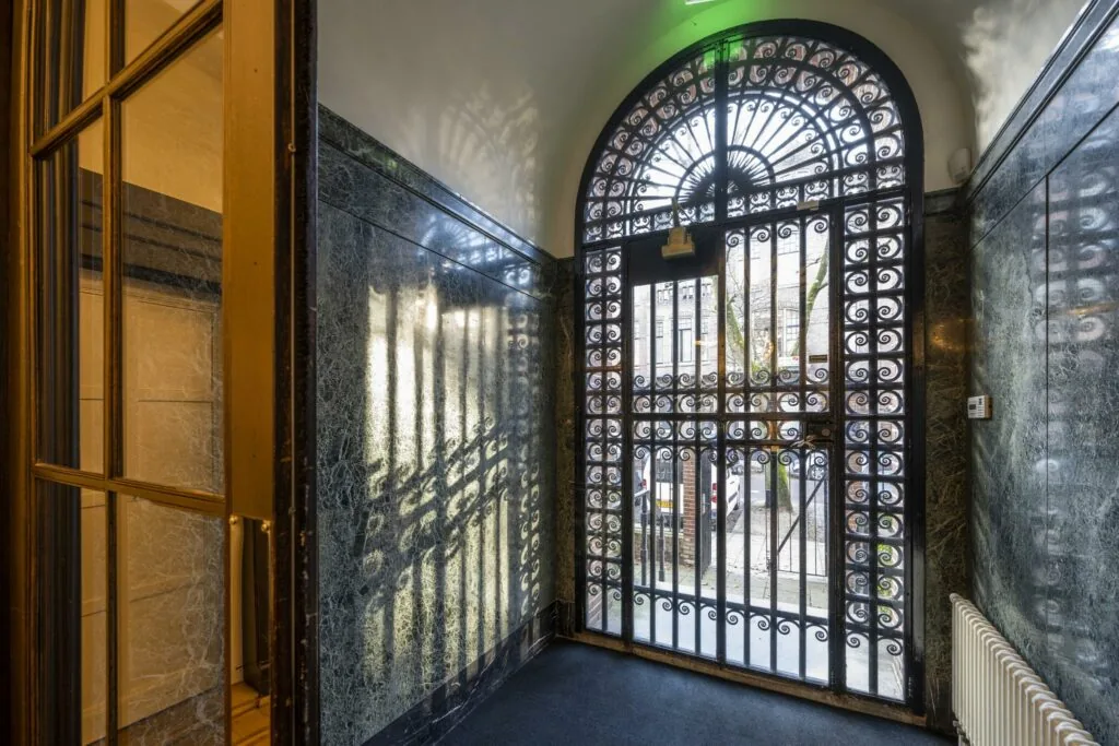 Binnenkomsthal met marmeren muren en een sierlijk smeedijzeren hek aan de Honthorststraat.