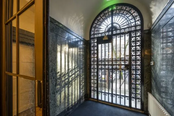 Binnenkomsthal met marmeren muren en een sierlijk smeedijzeren hek aan de Honthorststraat.