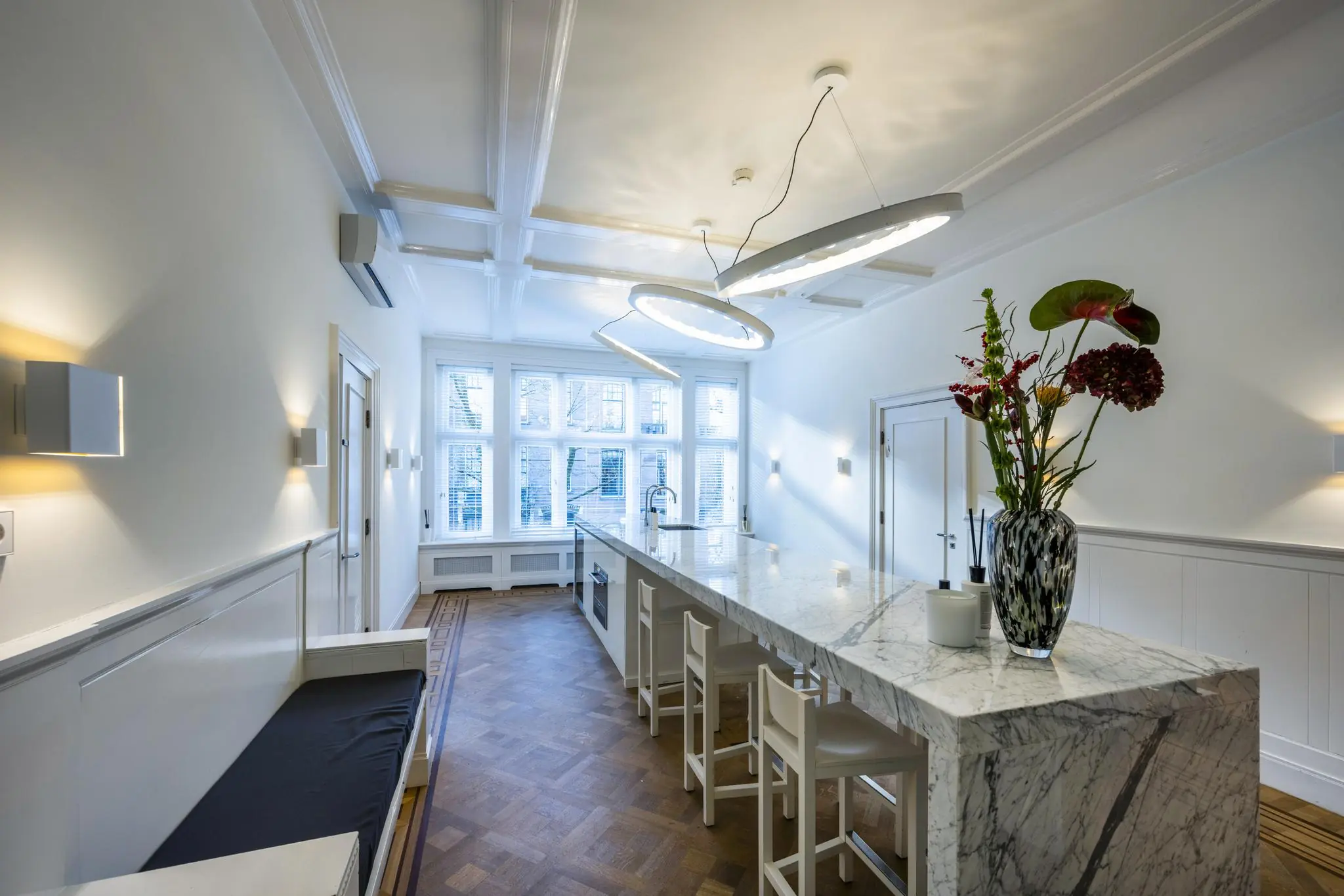 Moderne keuken aan de Honthorststraat met marmeren kookeiland, designverlichting en grote ramen.