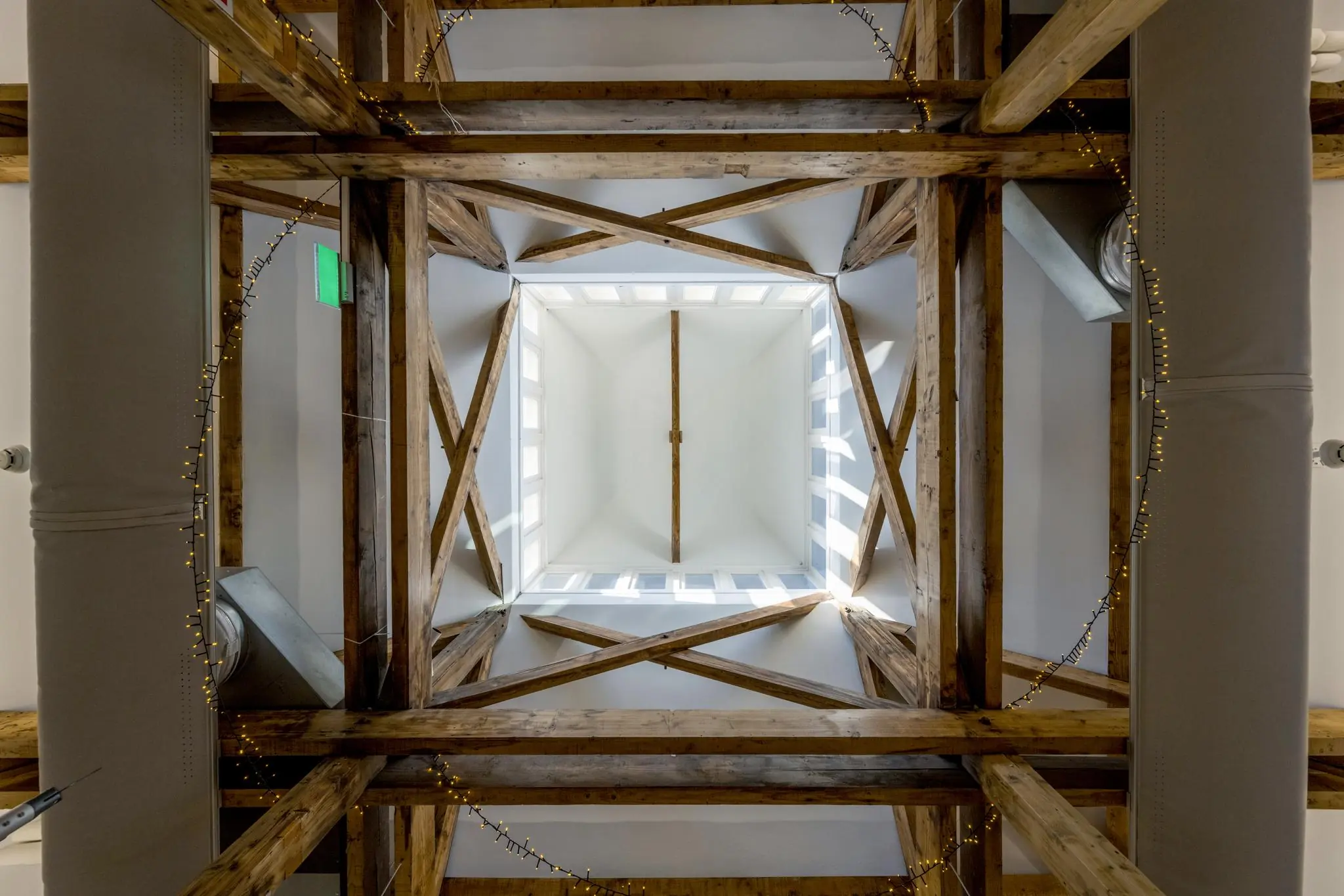 Doorkijk naar een vierkante lichtkoepel in het plafond met houten balken en sfeerverlichting aan het plafond van de Honthorststraat.