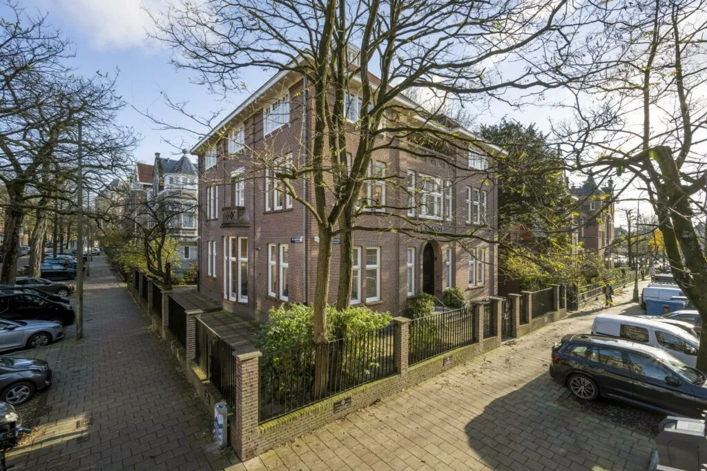 Hoekpand aan de Honthorststraat in Amsterdam, omgeven door bomen en geparkeerde auto's op een zonnige dag.