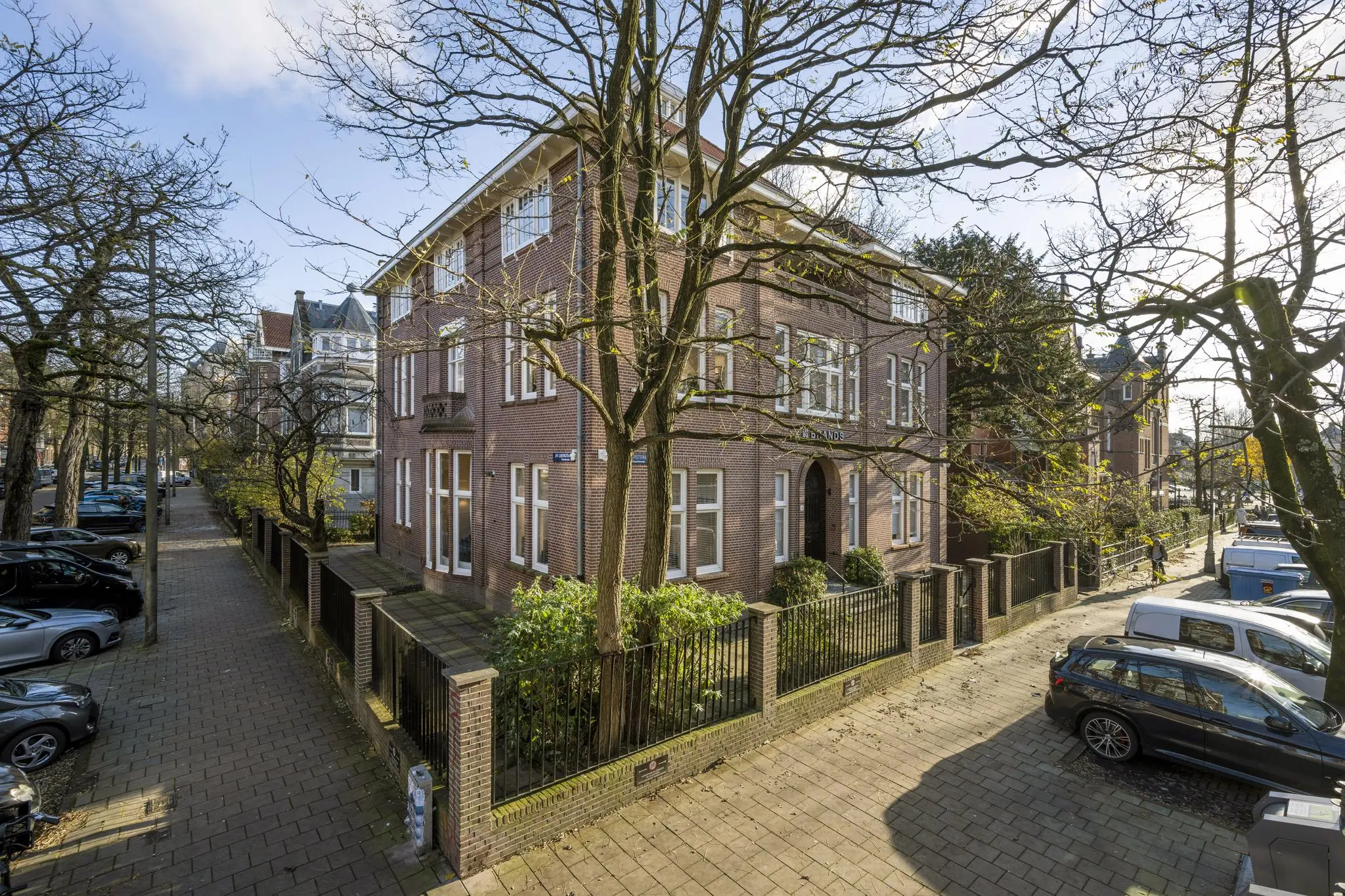 Hoekpand aan de Honthorststraat in Amsterdam, omgeven door bomen en geparkeerde auto's op een zonnige dag.
