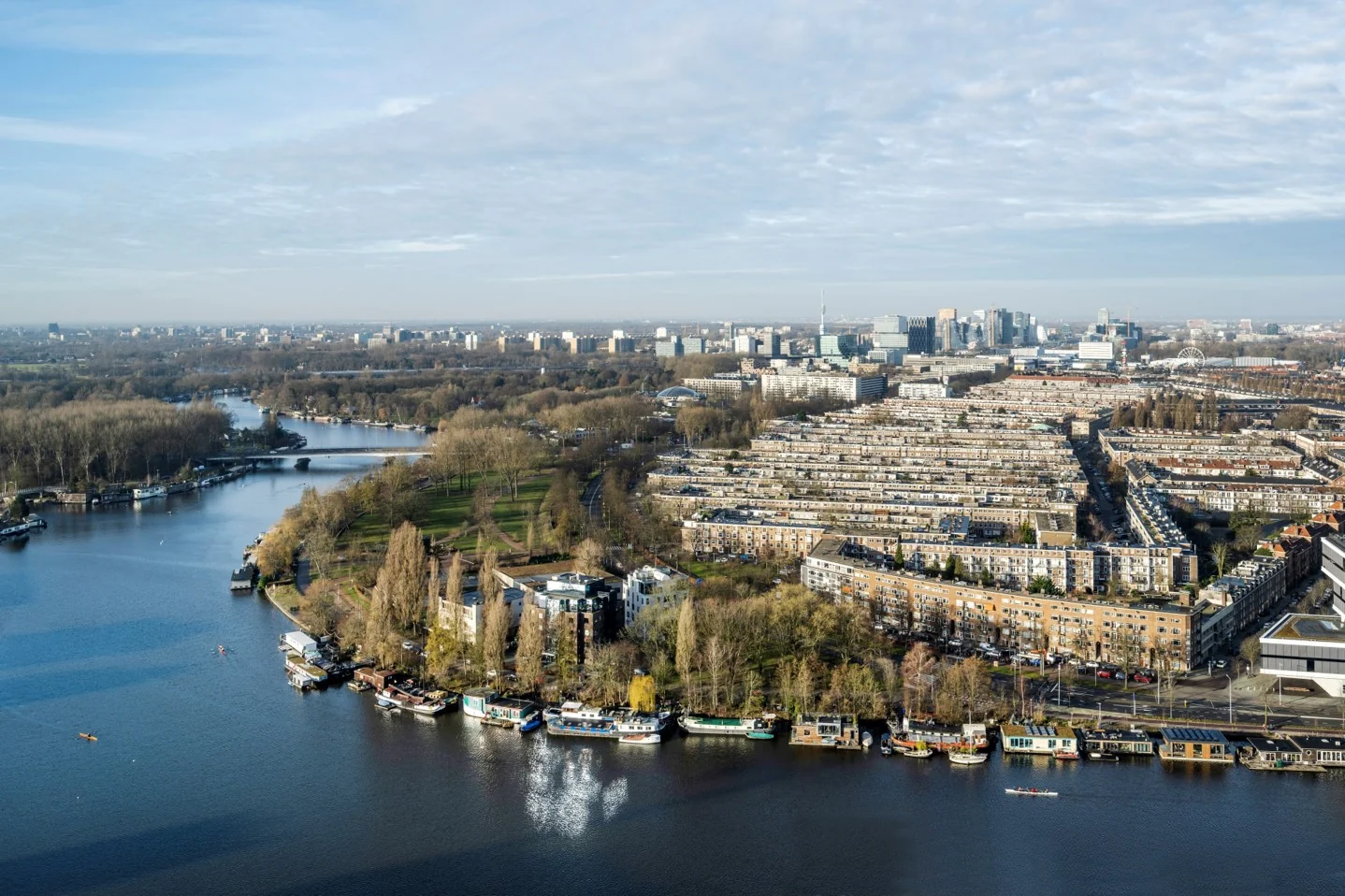 Luchtfoto van Amstelplein in Amsterdam met zicht op woonboten, het park langs de Amstel en de stedelijke bebouwing op de achtergrond.