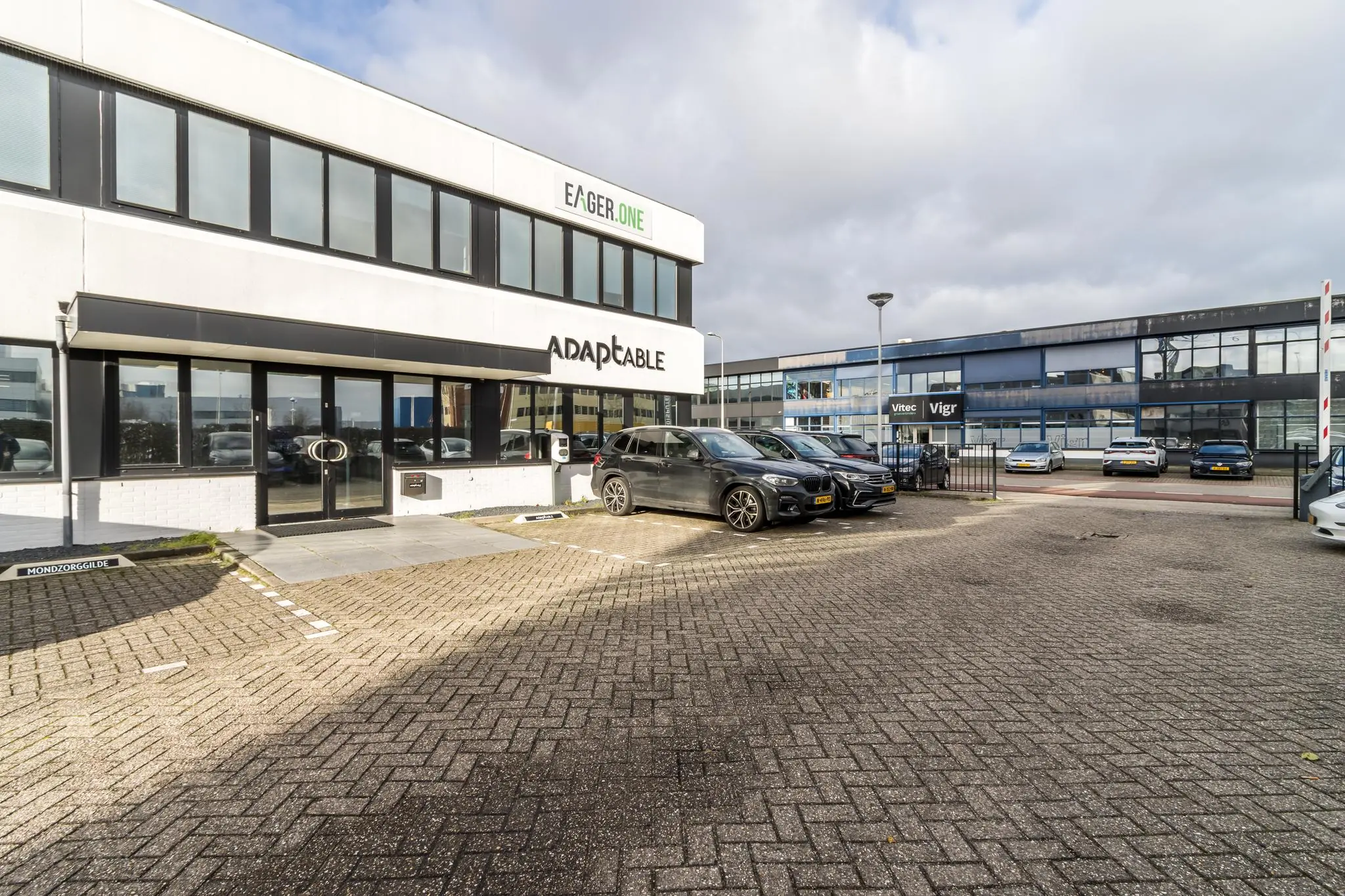 Bedrijfsgebouwen aan de Savannahweg met geparkeerde auto's op de parkeerplaats voor Adaptable, Eager.One en Vitec/Vigr.