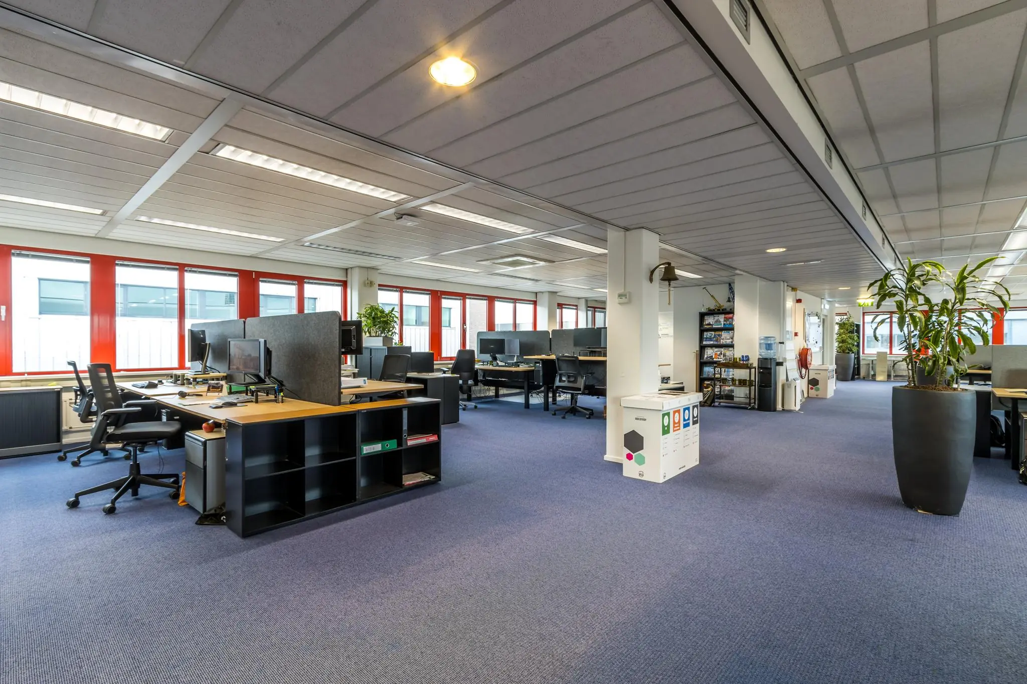 Ruim en modern kantoorinterieur aan de Savannahweg met werkplekken, planten en rode raamkozijnen.
