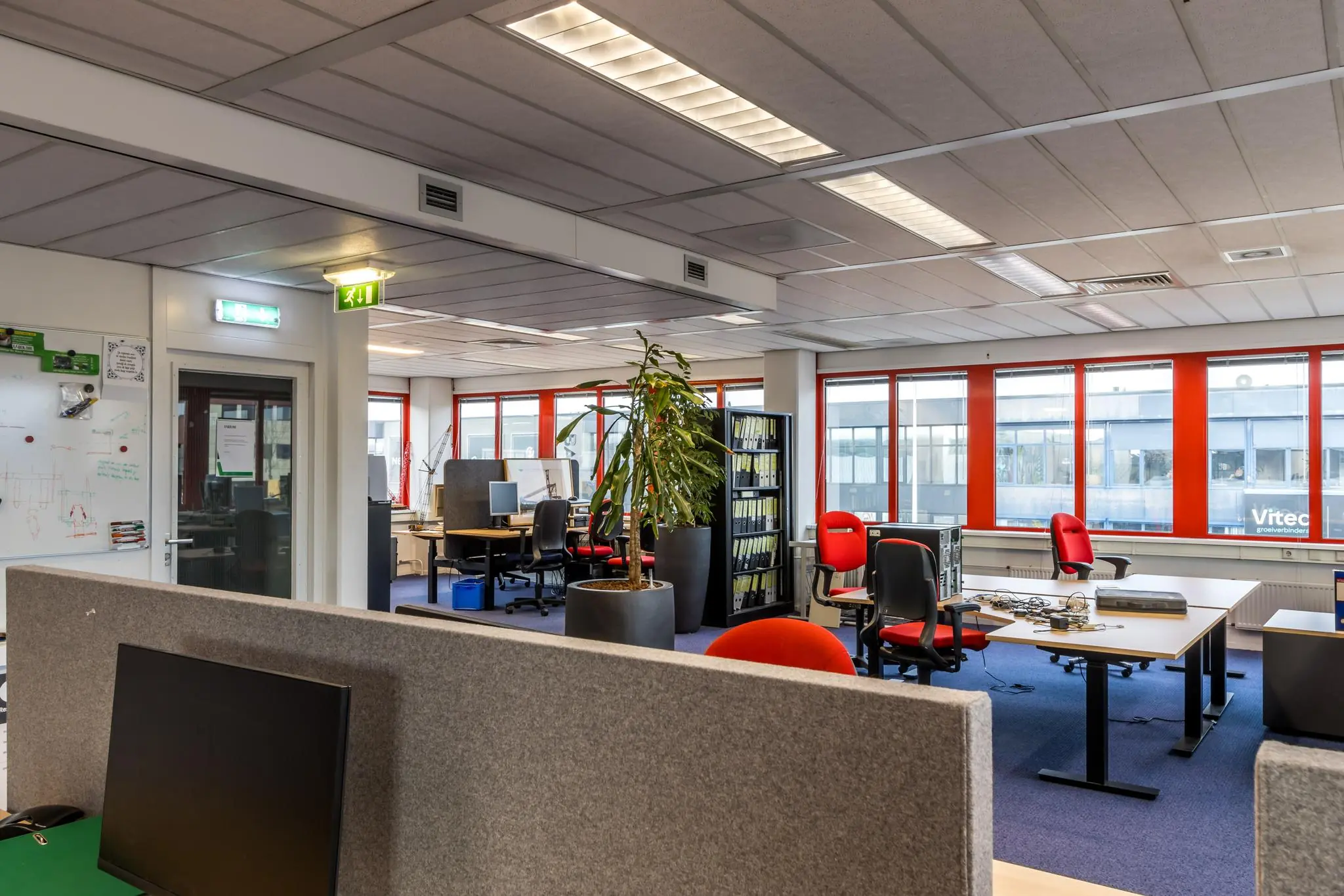 Modern kantoorpand aan de Savannahweg met meerdere werkplekken, rode bureaustoelen en grote ramen met uitzicht op Vitec.