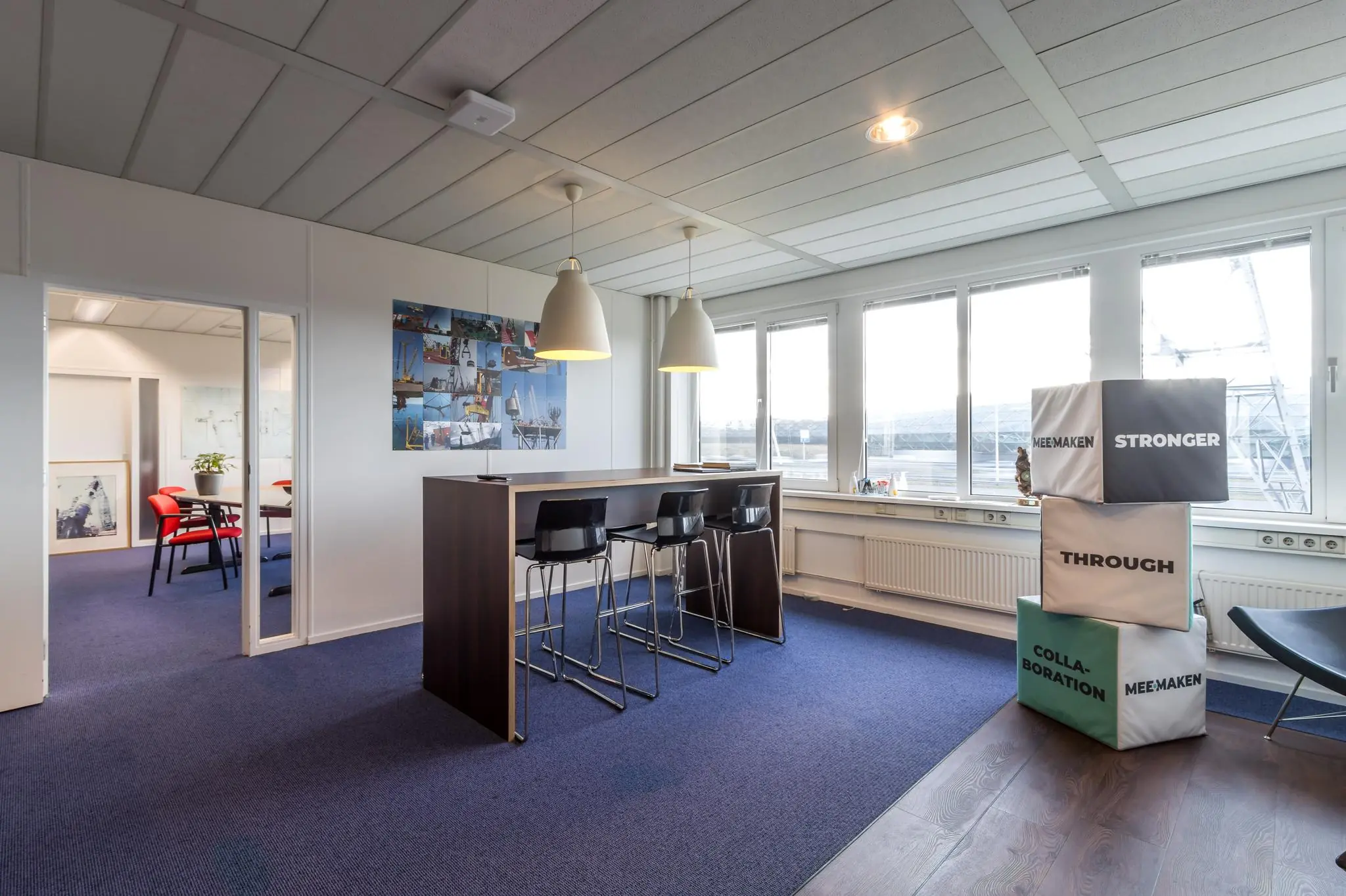 Moderne kantoorruimte aan de Savannahweg met hoge tafel, barkrukken, fotocollage en blokken met inspirerende teksten bij het raam.