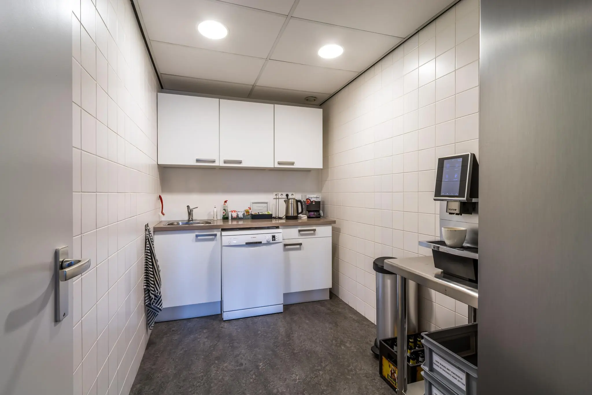 Kleine, functionele pantry met witte kasten, een koffieautomaat en een vaatwasser aan de Savannahweg.